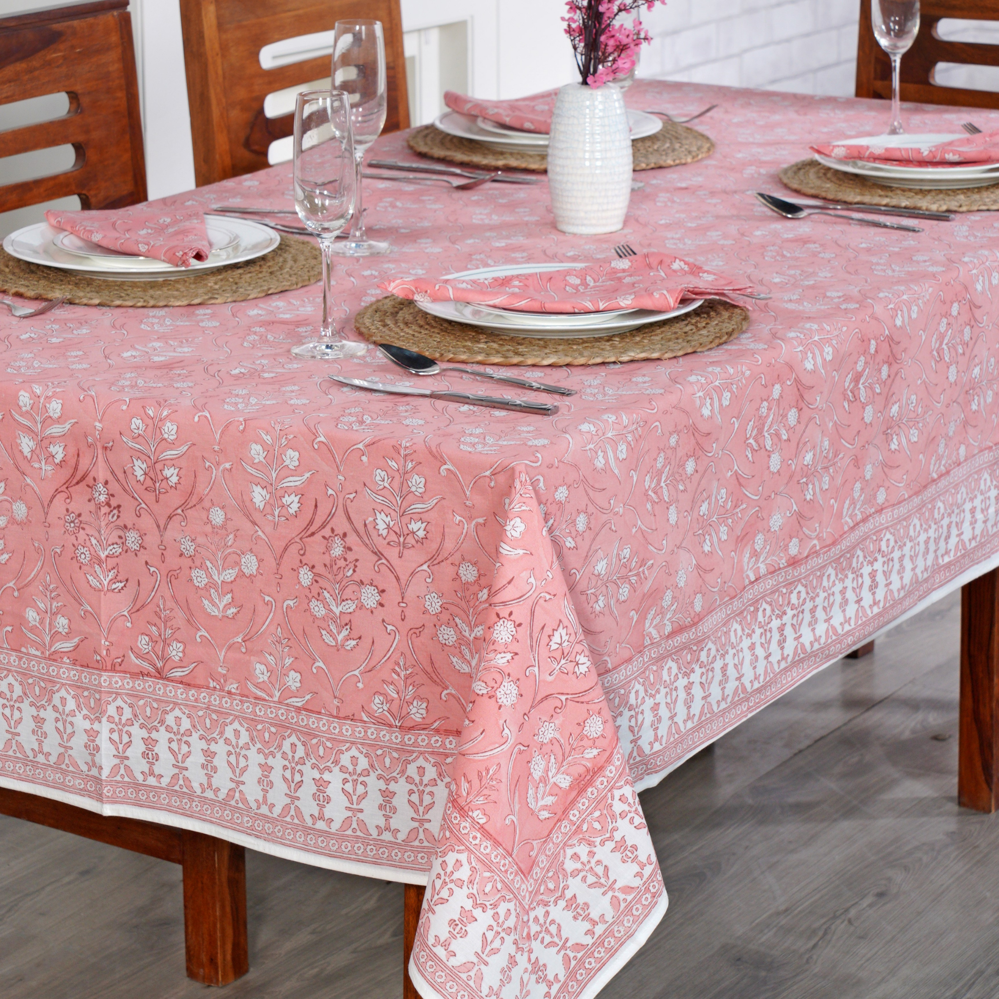 Dining table set with a pink floral tablecloth, plates, cutlery, and glasses.