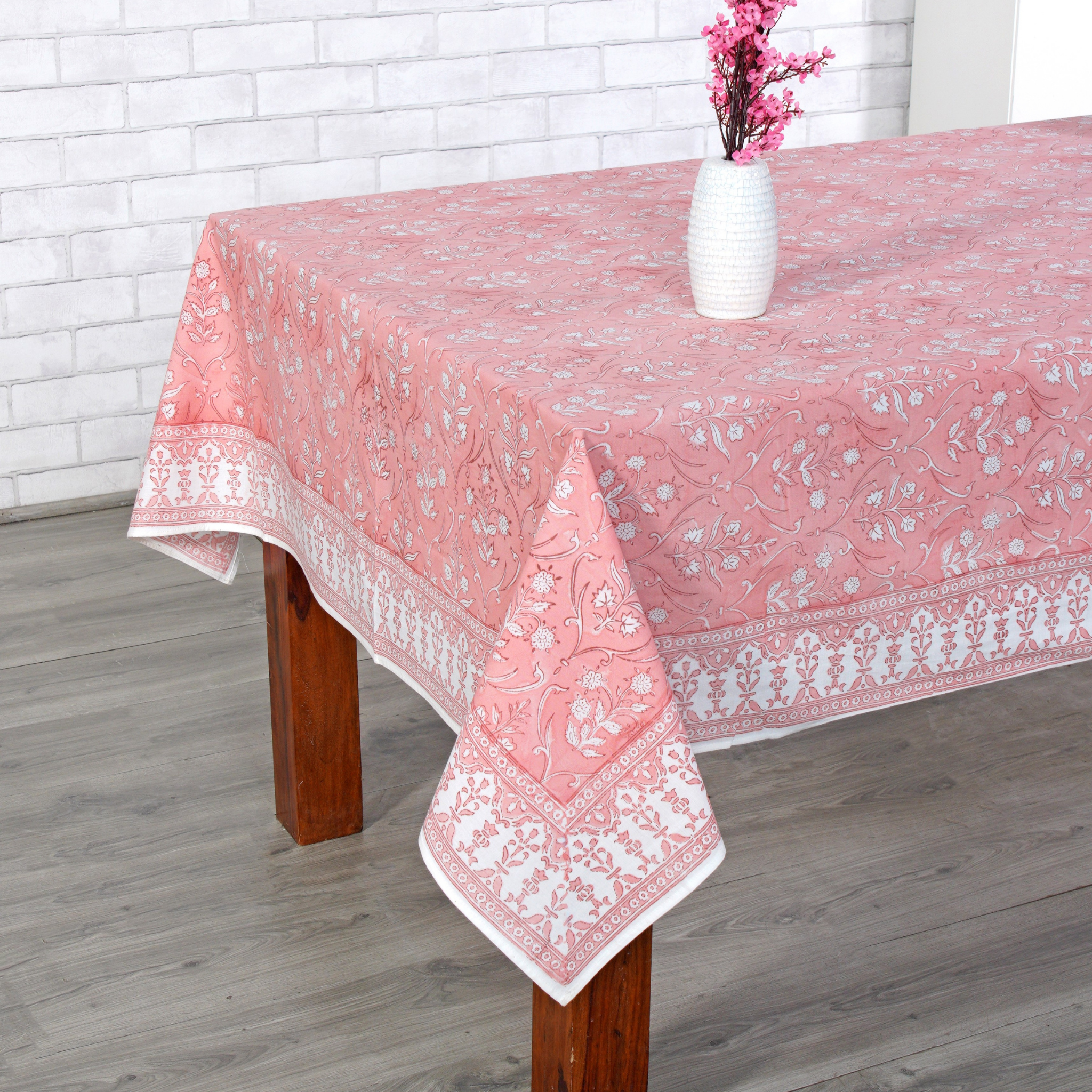 Pink tablecloth with white lace patterns on a wooden table against a white brick wall.