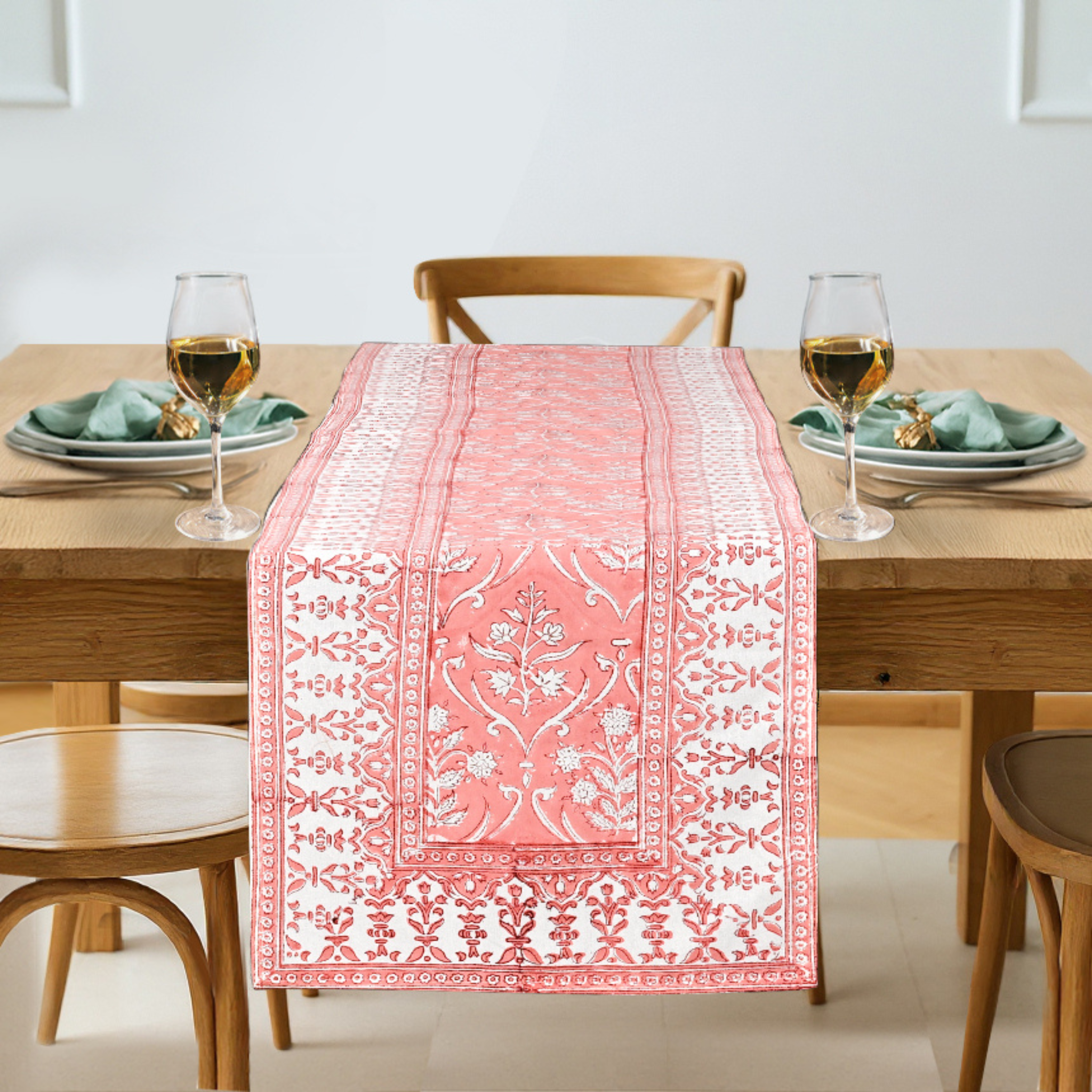 Dining table set with a pink patterned table runner, glasses, and plates.