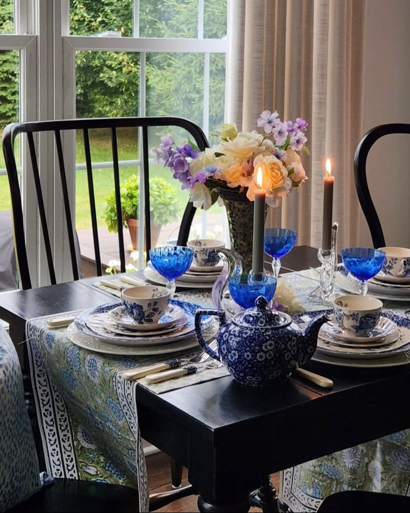 Dining room with a black table set for a meal, featuring blue and white dishes and a chandelier.