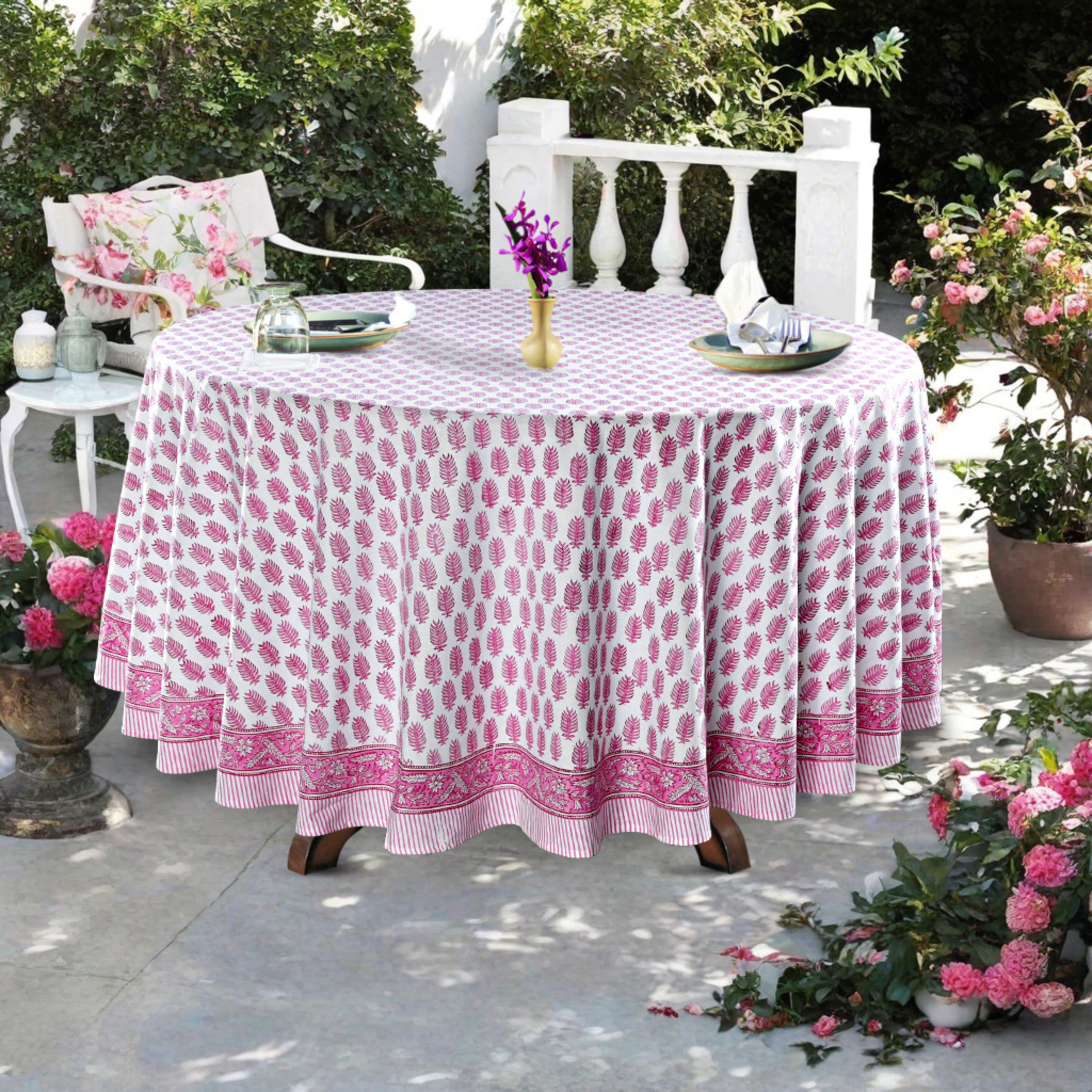 Round table with a pink and white patterned tablecloth outdoors.