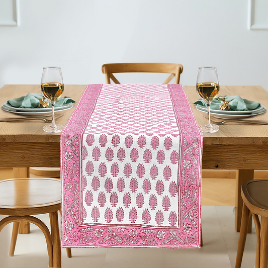 Dining table with a pink and white patterned table runner, glasses, and plates.