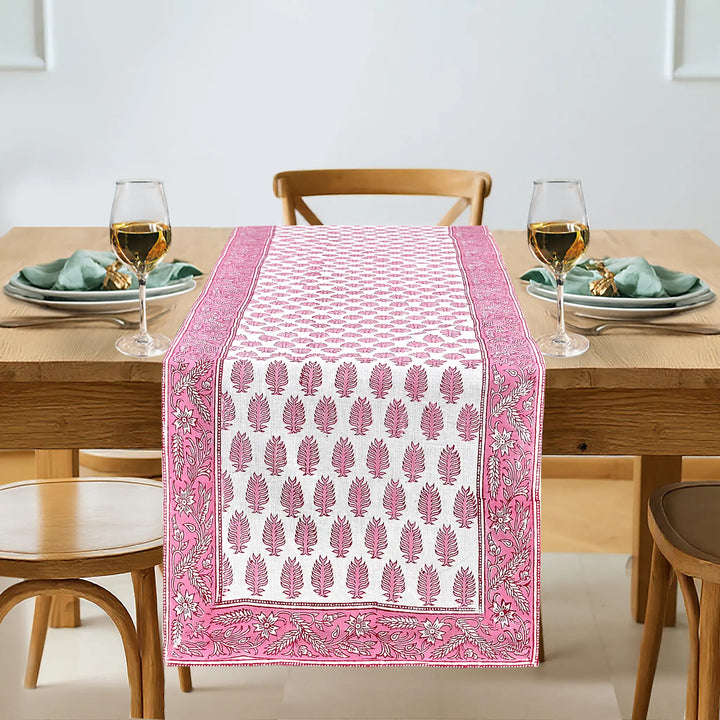 Dining table with a pink and white patterned table runner, glasses, and plates.