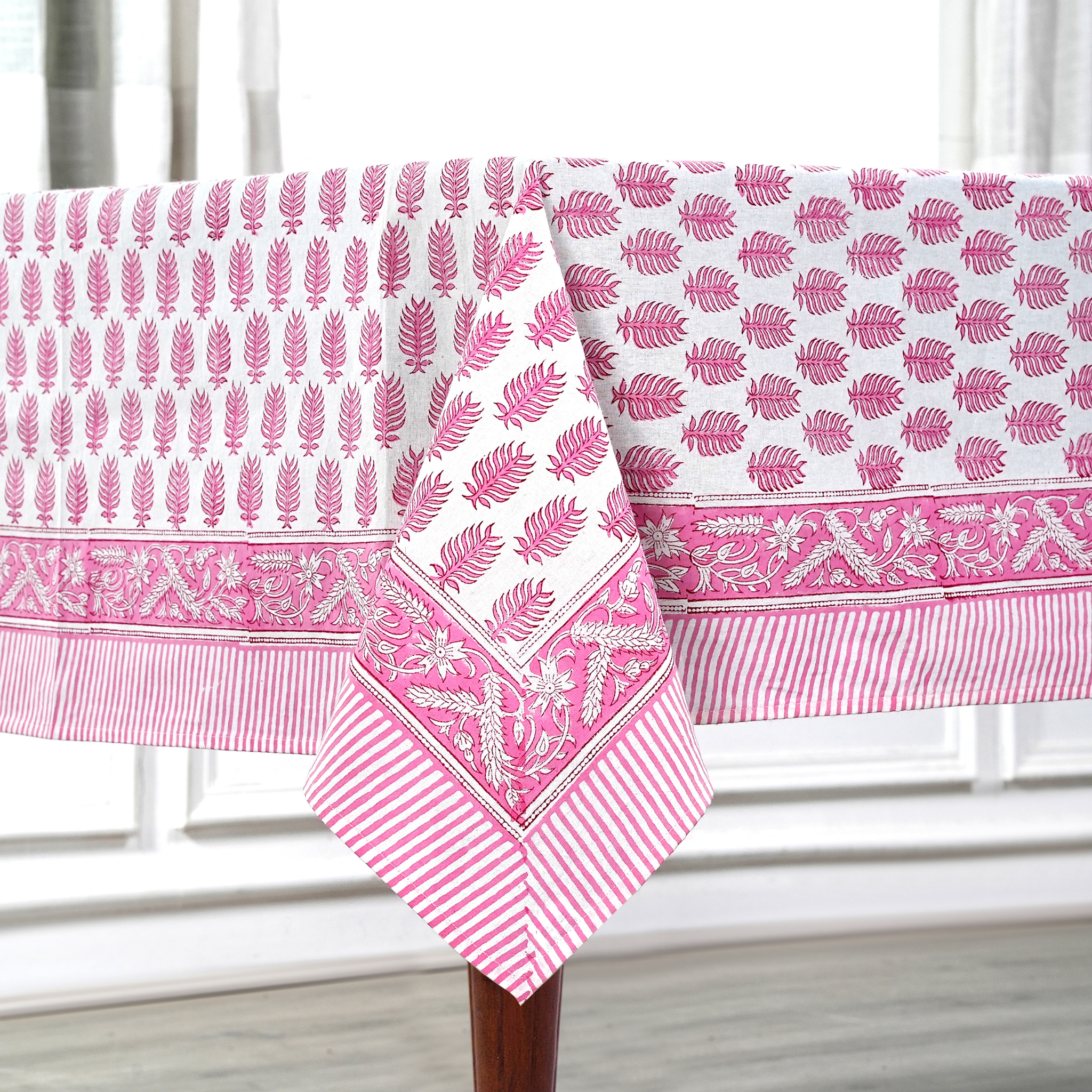 Pink and white patterned tablecloth on a wooden table with a white curtain background
