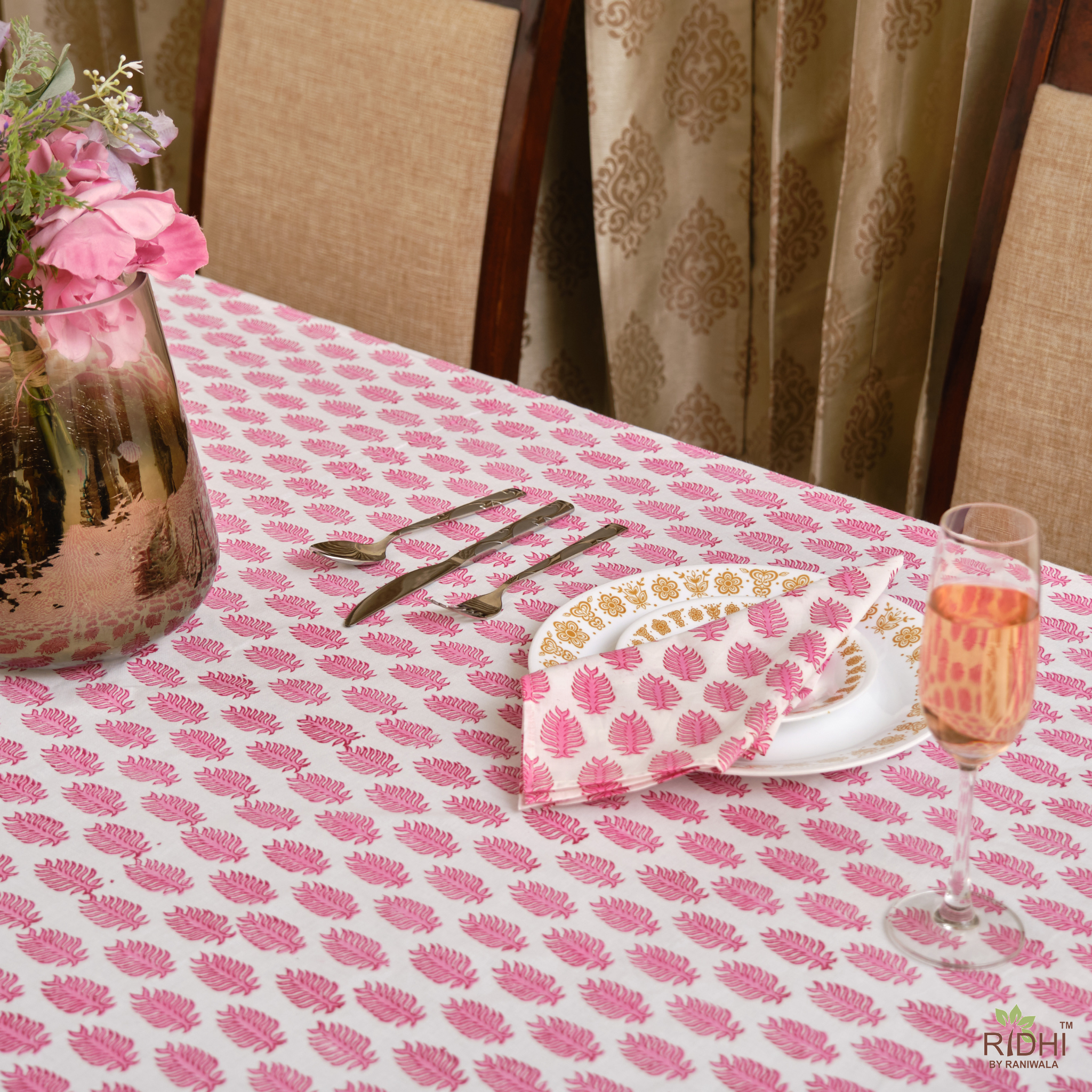 Table setting with pink floral tablecloth, plates, cutlery, and a glass of water.
