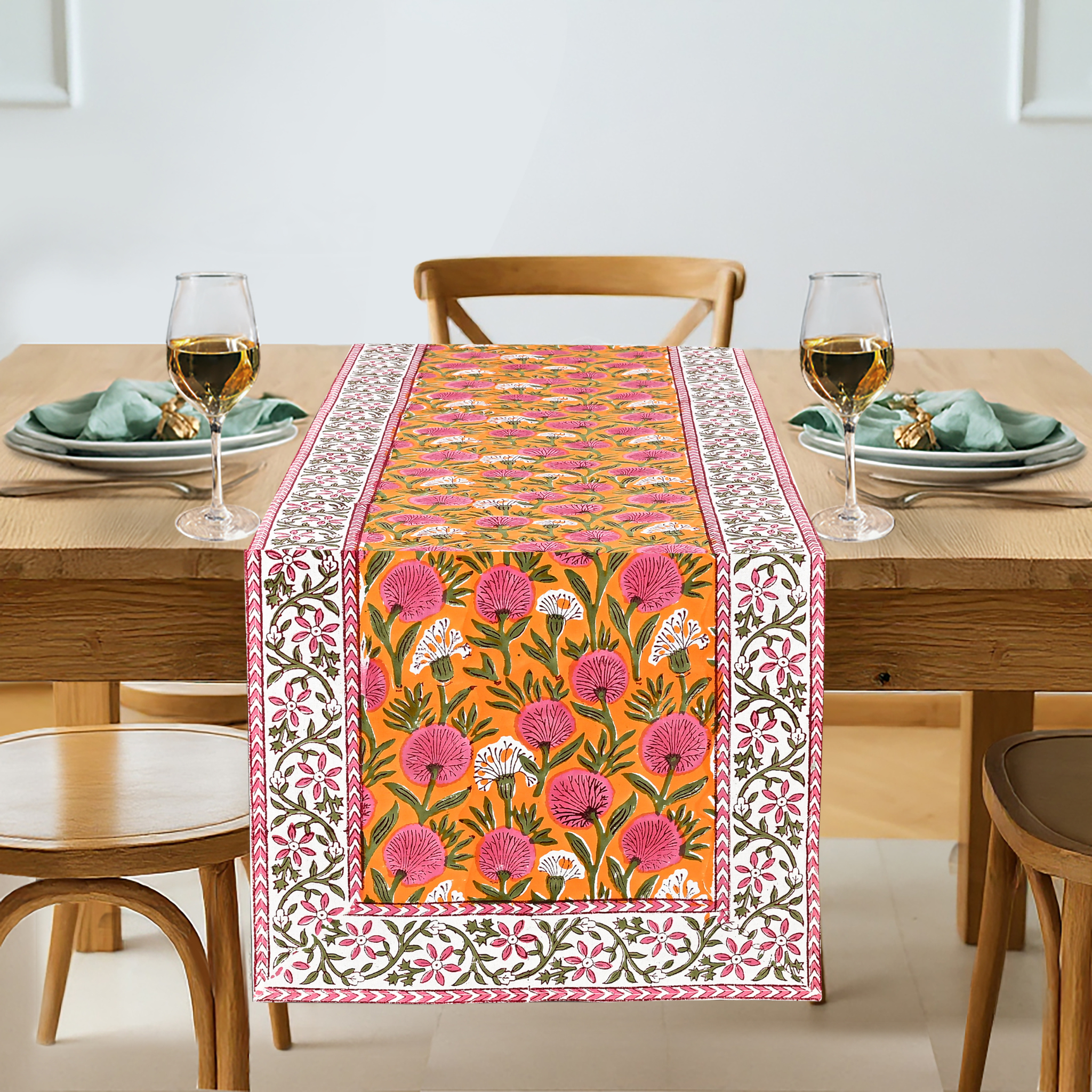 Dining table with a floral patterned table runner, glasses, and plates.