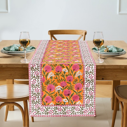 Dining table with a floral patterned table runner, glasses, and plates.