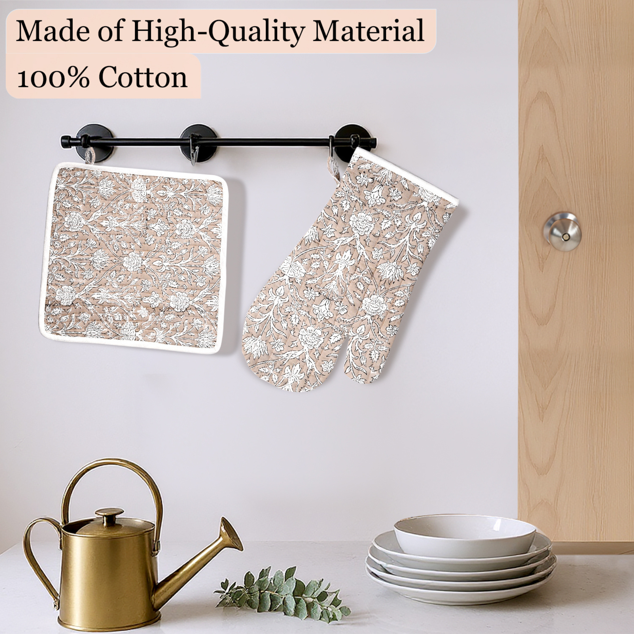 Floral-patterned pot holder and trivet hanging on a kitchen wall with a gold watering can and white bowls below.