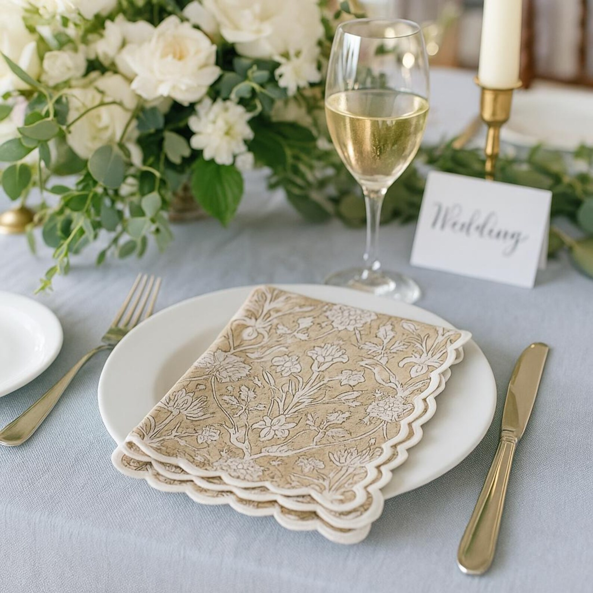 Wedding table setting with floral napkins, wine glass, and place card.