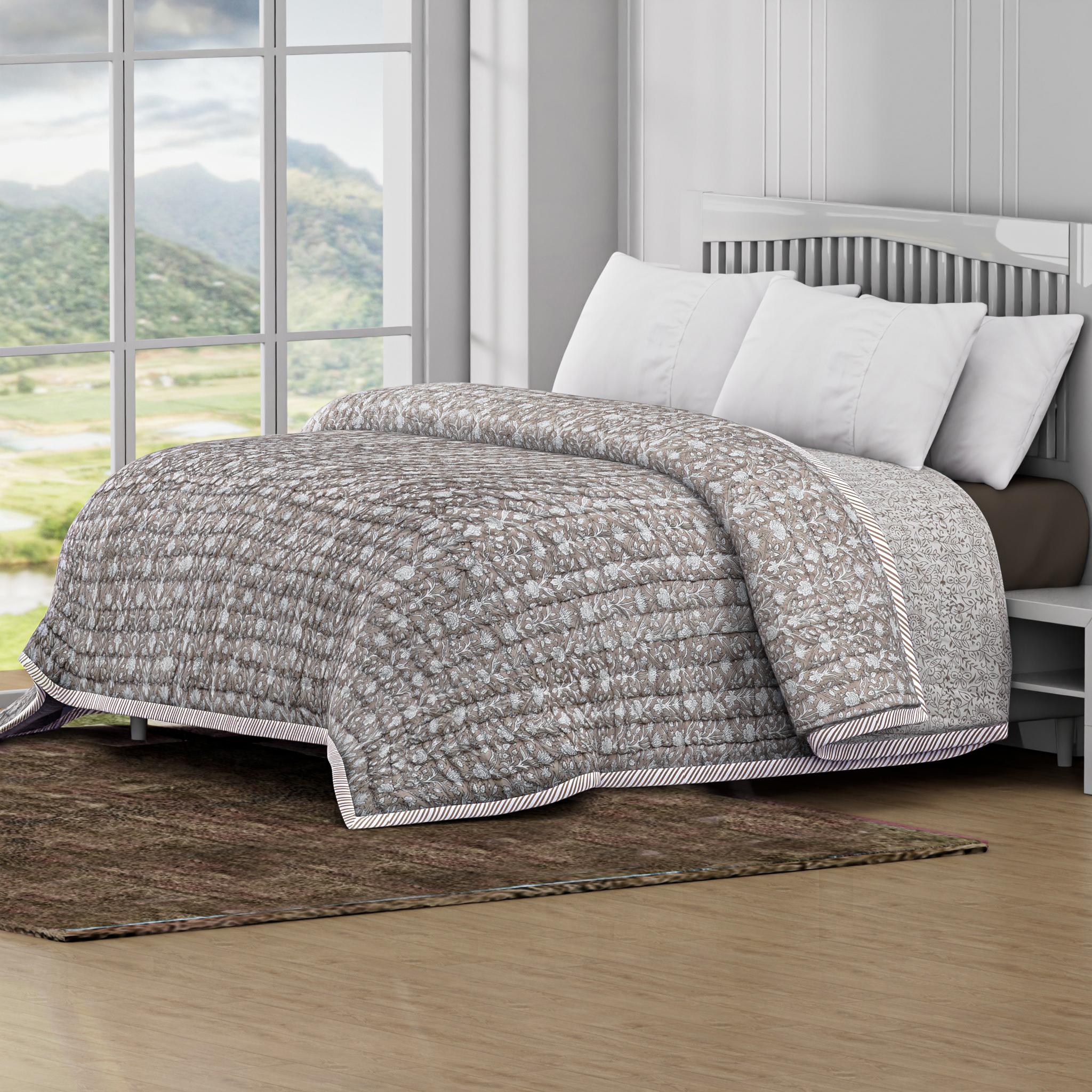 Bed with gray quilt and white pillows in a room with large windows showing a scenic view.