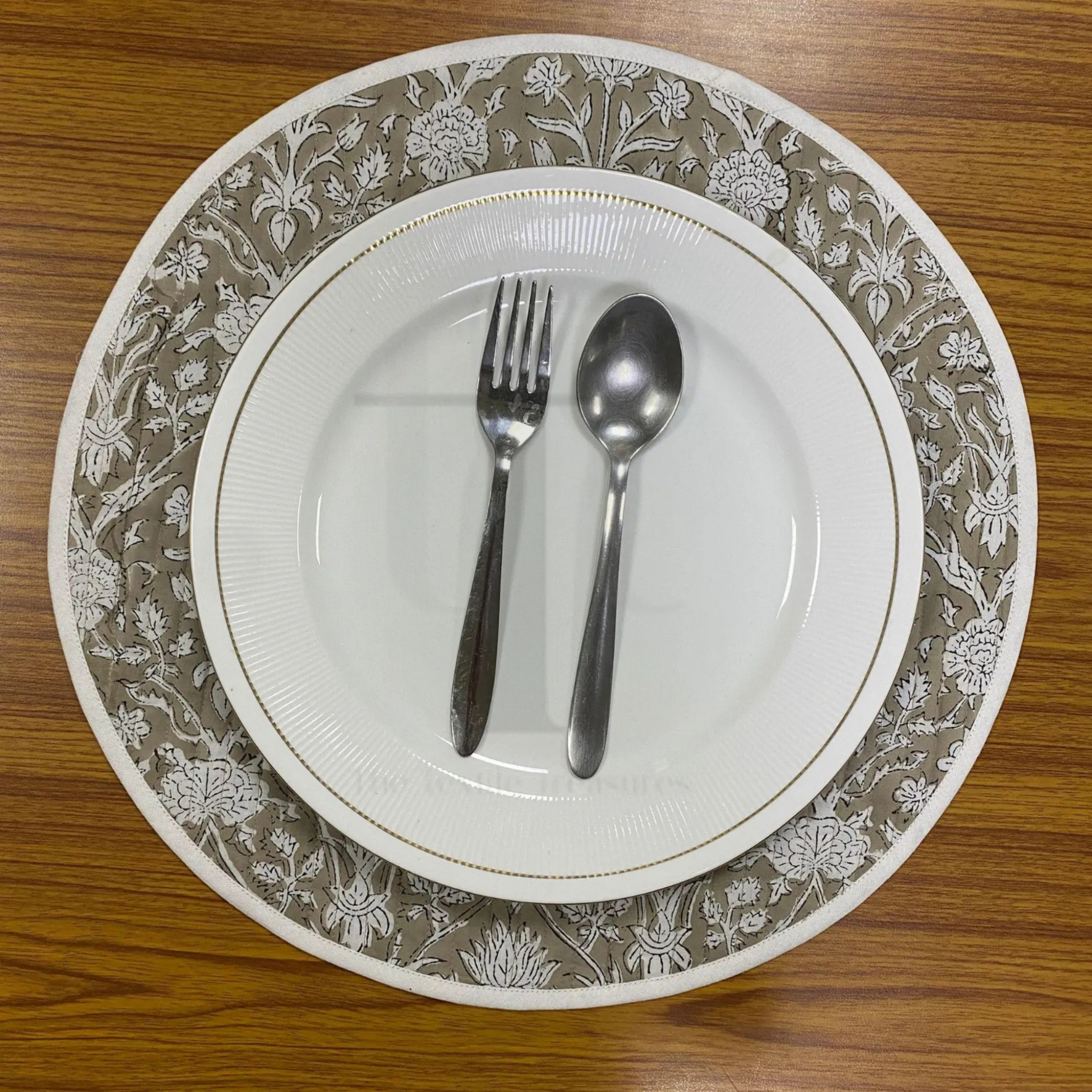 White plate with floral rim, silver fork, and spoon on a wooden table.