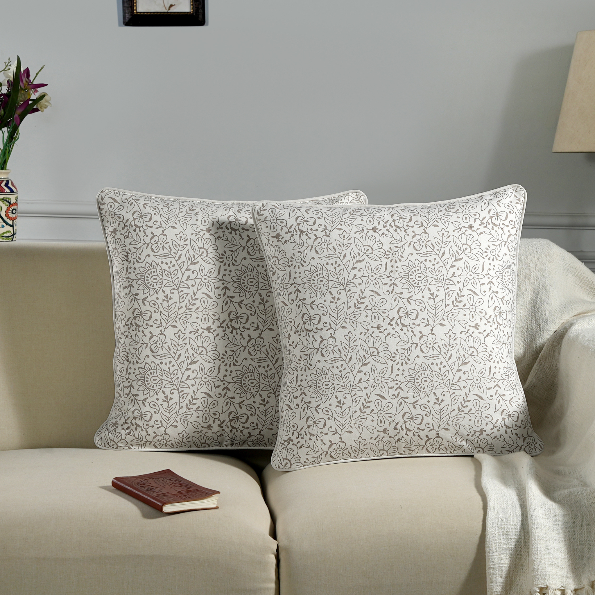 Two patterned pillows on a beige sofa with a small book and decorative vase in the background.