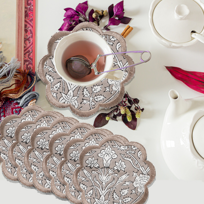 Set of lace coasters with a cup of tea and teapot on a table.