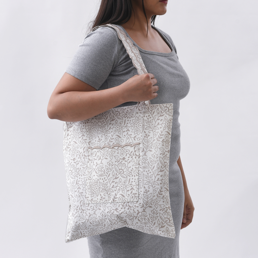 Person wearing a gray shirt with a white patterned tote bag over their shoulder on a plain background