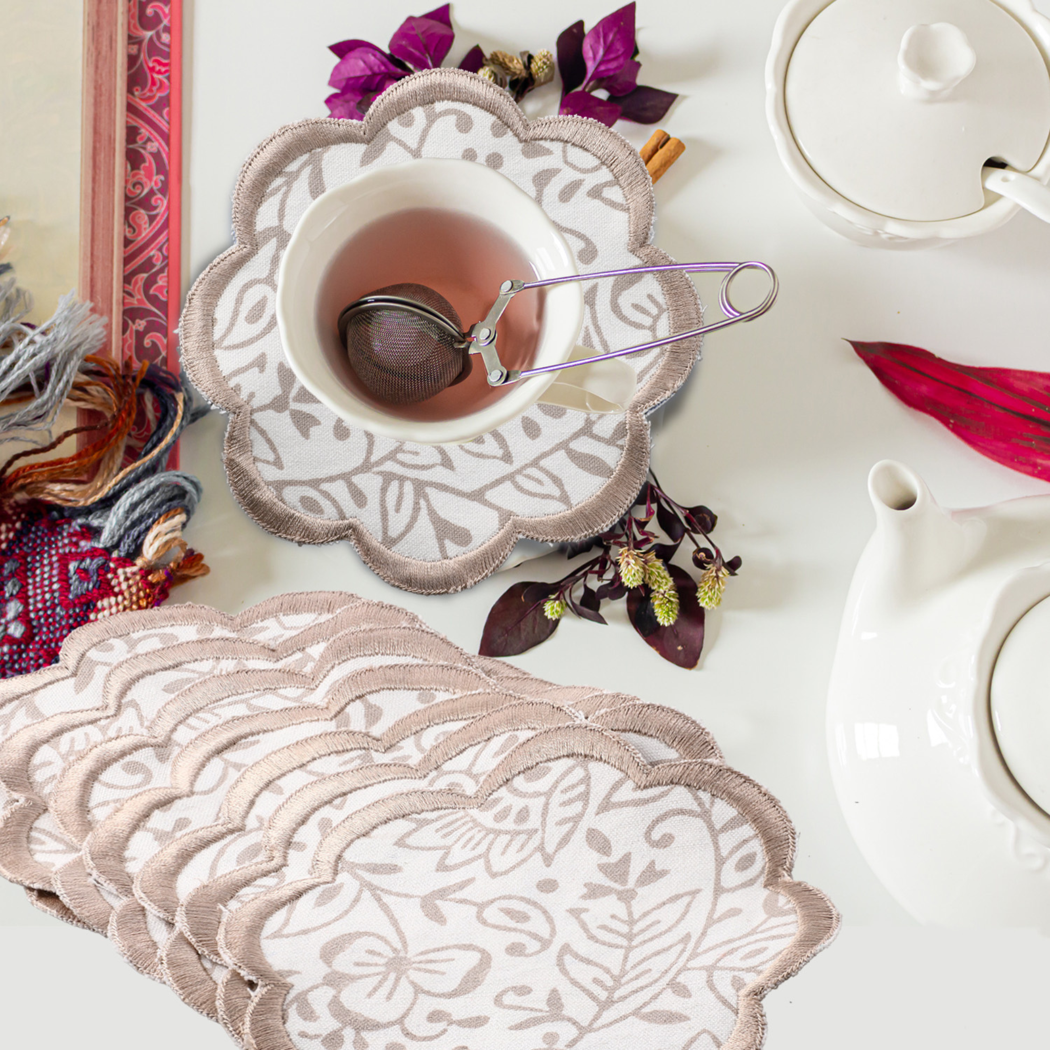 Decorative lace coasters with a cup of tea and teapot on a white surface.