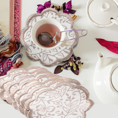 Decorative lace coasters with a cup of tea and teapot on a white surface.