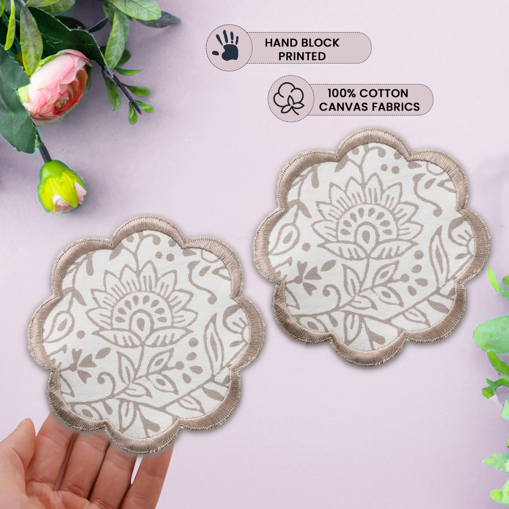 Two floral-patterned coasters held by a hand with greenery in the background, labeled as hand block printed and 100% cotton canvas fabrics.