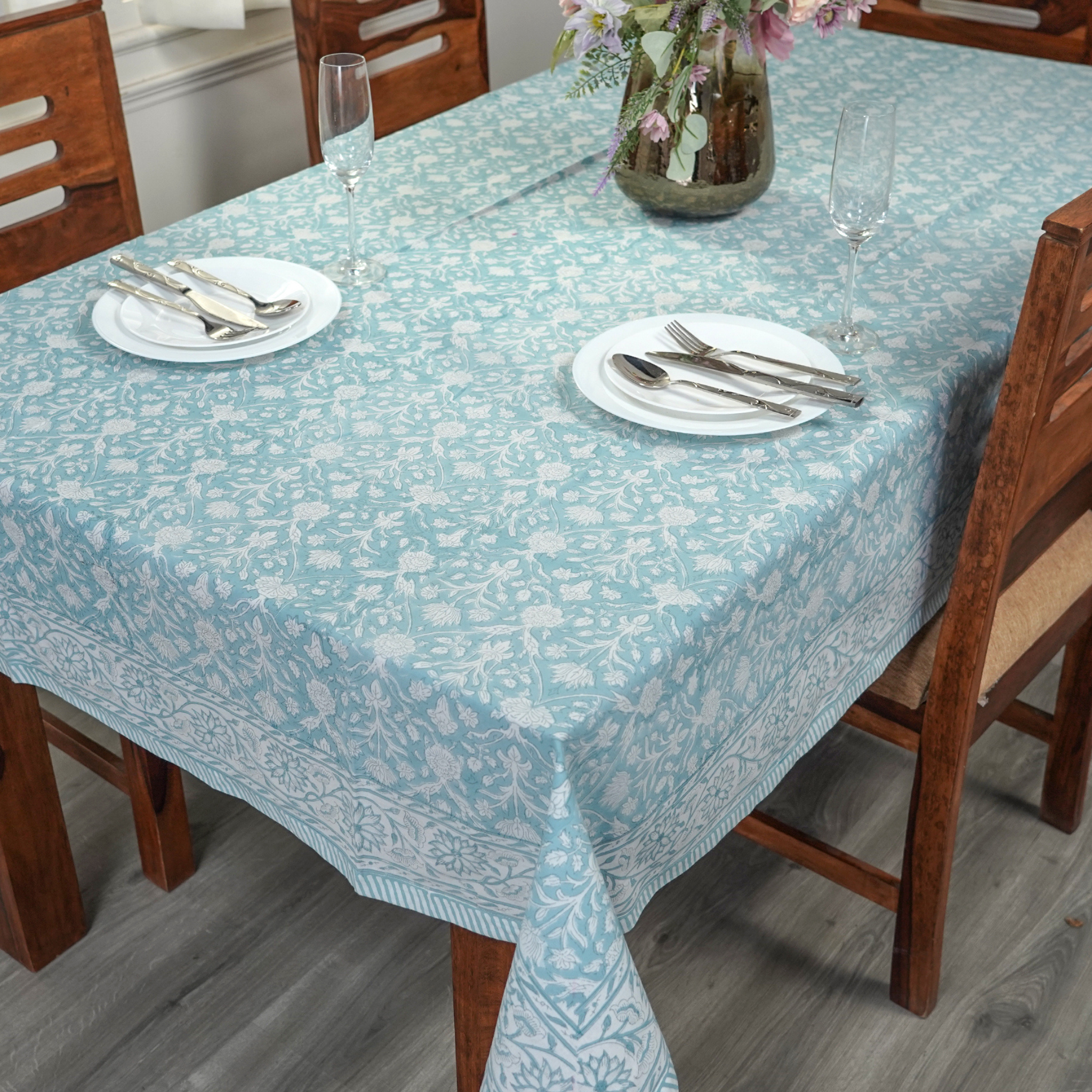 Dining table set with a floral-patterned tablecloth, plates, and cutlery.