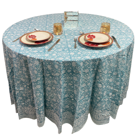 Round table with a floral patterned tablecloth, plates, cutlery, and glasses on a white background