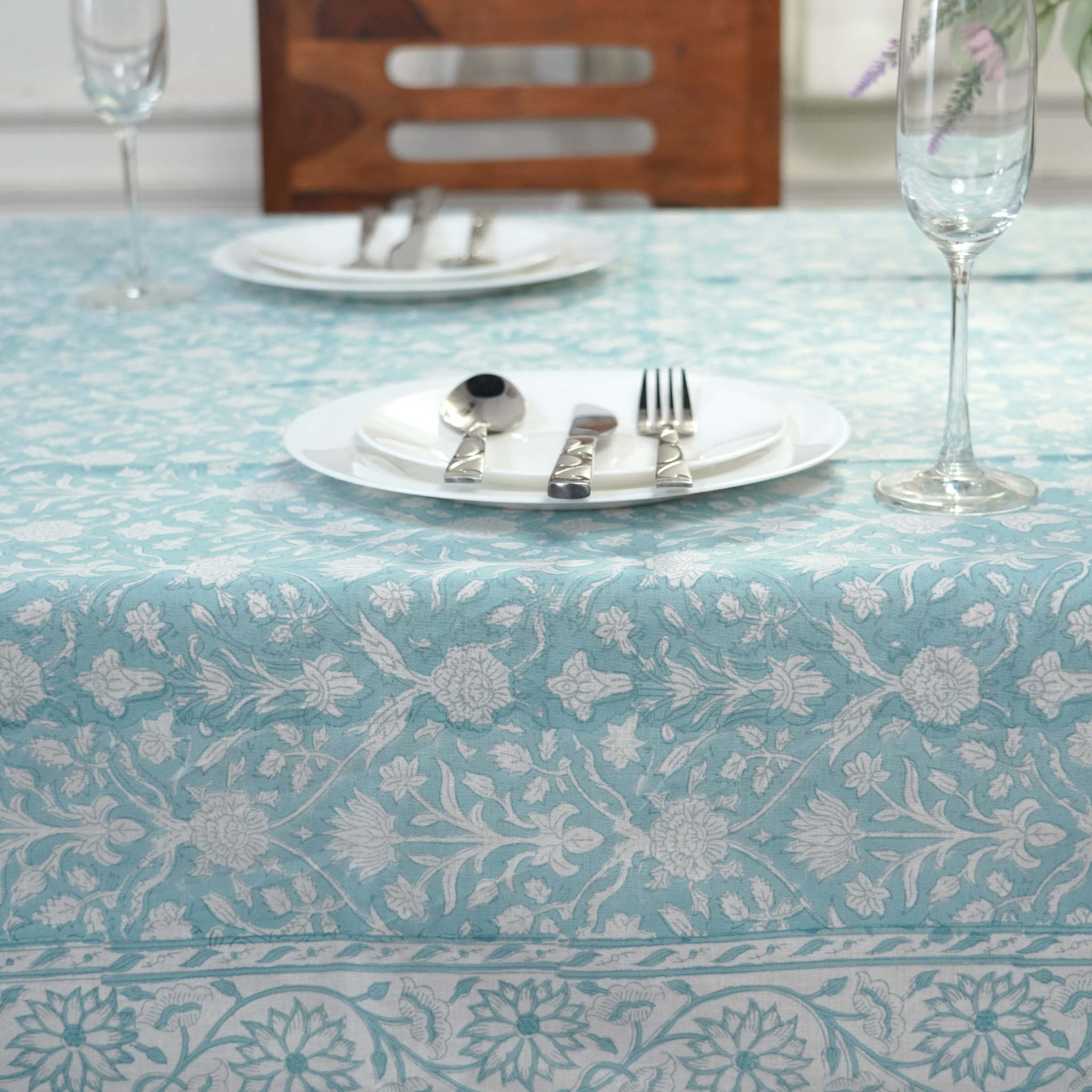 Table setting with floral-patterned tablecloth, plates, cutlery, and glasses.