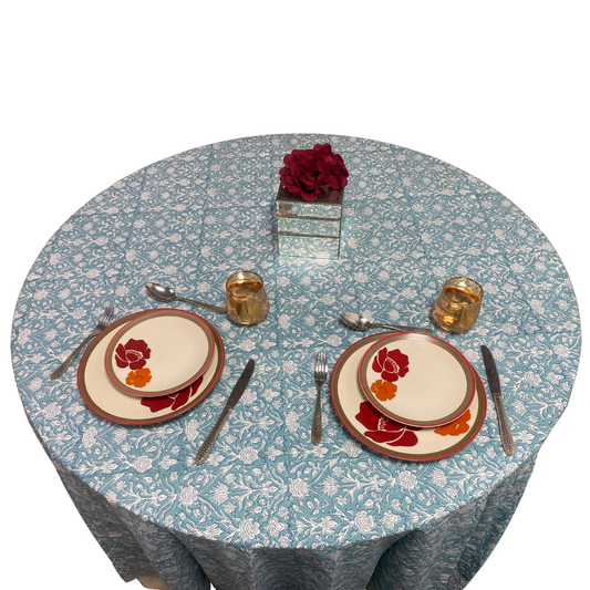 Round table with floral tablecloth, plates, cutlery, and centerpieces on a white background