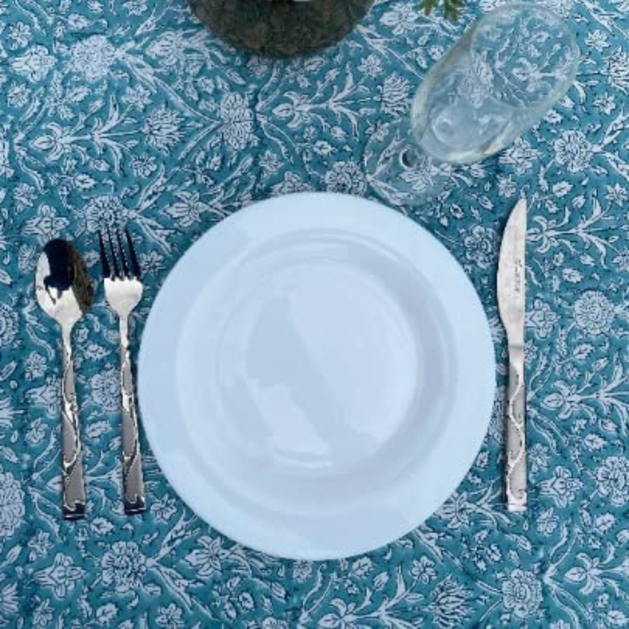 White plate with silverware on a blue floral tablecloth
