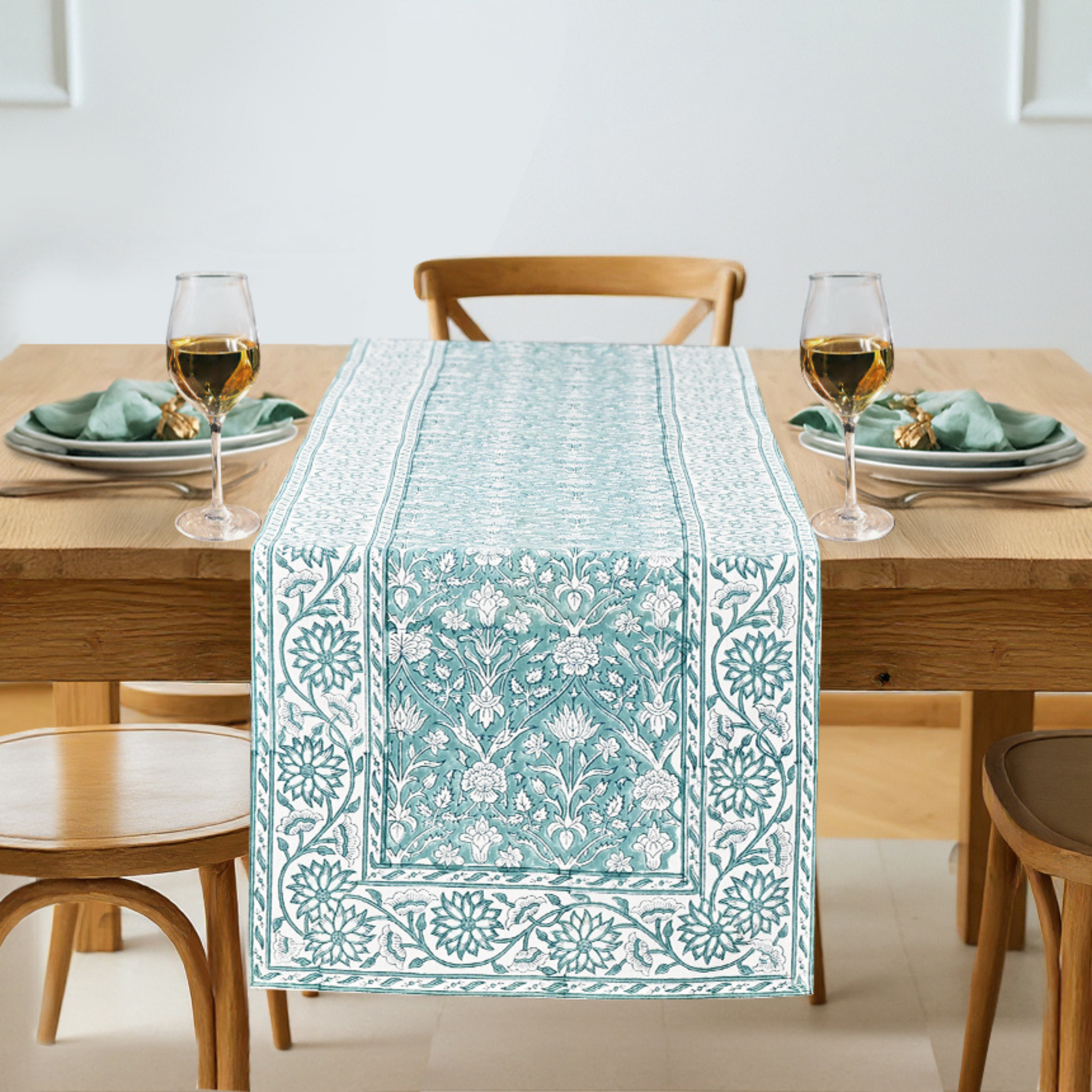 Teal patterned table runner on a wooden table with glasses and plates.