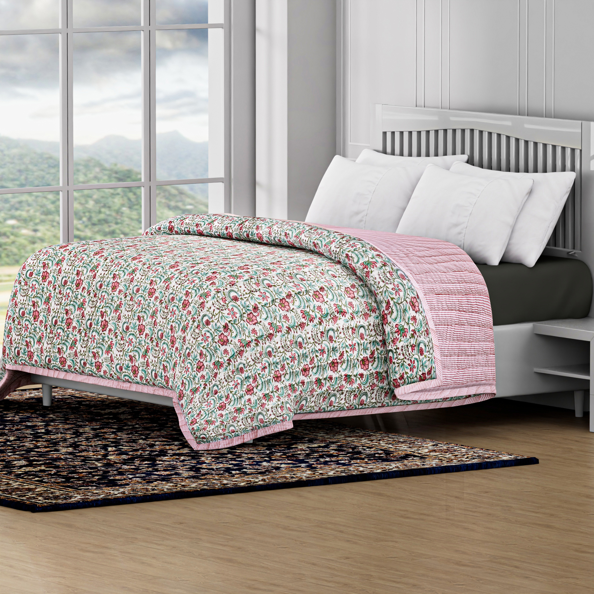 Floral quilt with pink border on a bed in a room with large windows.
