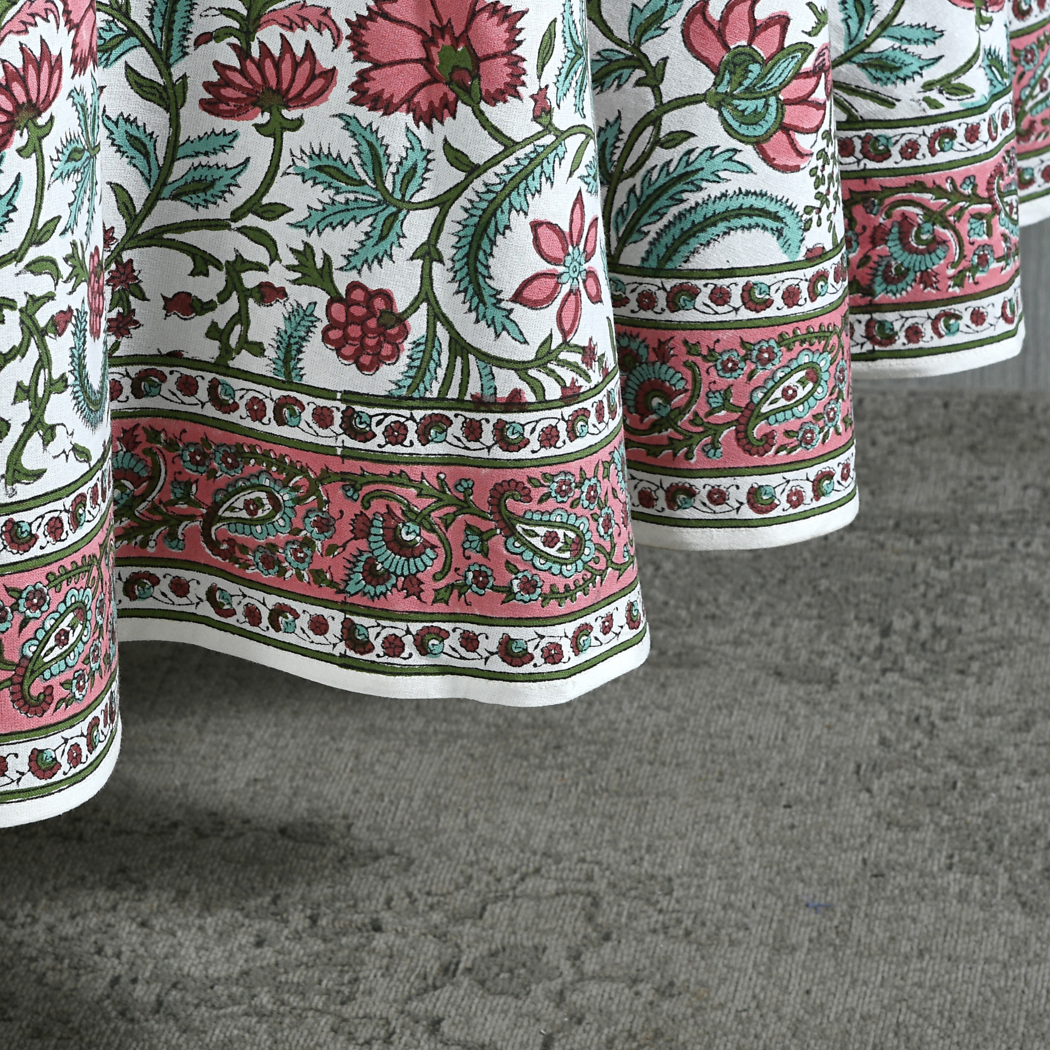 Close-up of a floral patterned fabric with pink, green, and red colors on a gray surface.