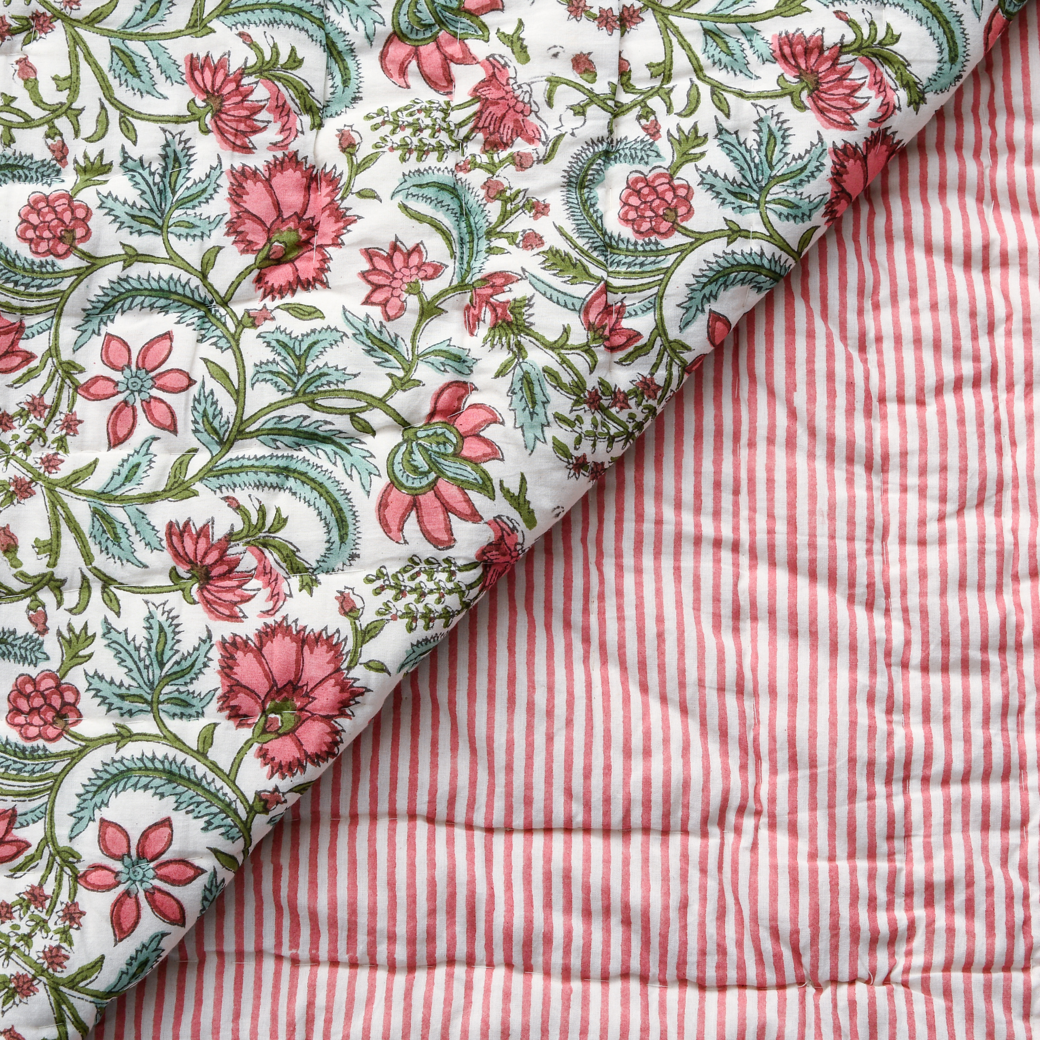 Floral fabric with pink flowers and green leaves on a white background, folded over red and white striped fabric.