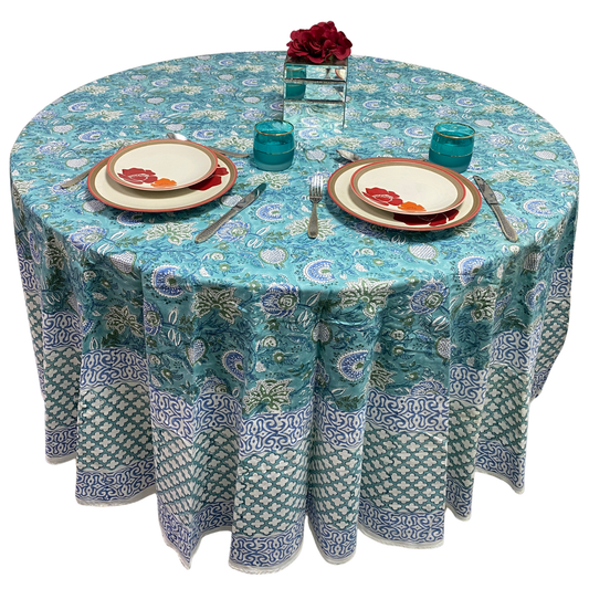 Round table with a patterned blue tablecloth, plates, and cutlery on a white background