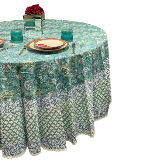 Round table with a patterned teal and white tablecloth, set with plates and glasses.