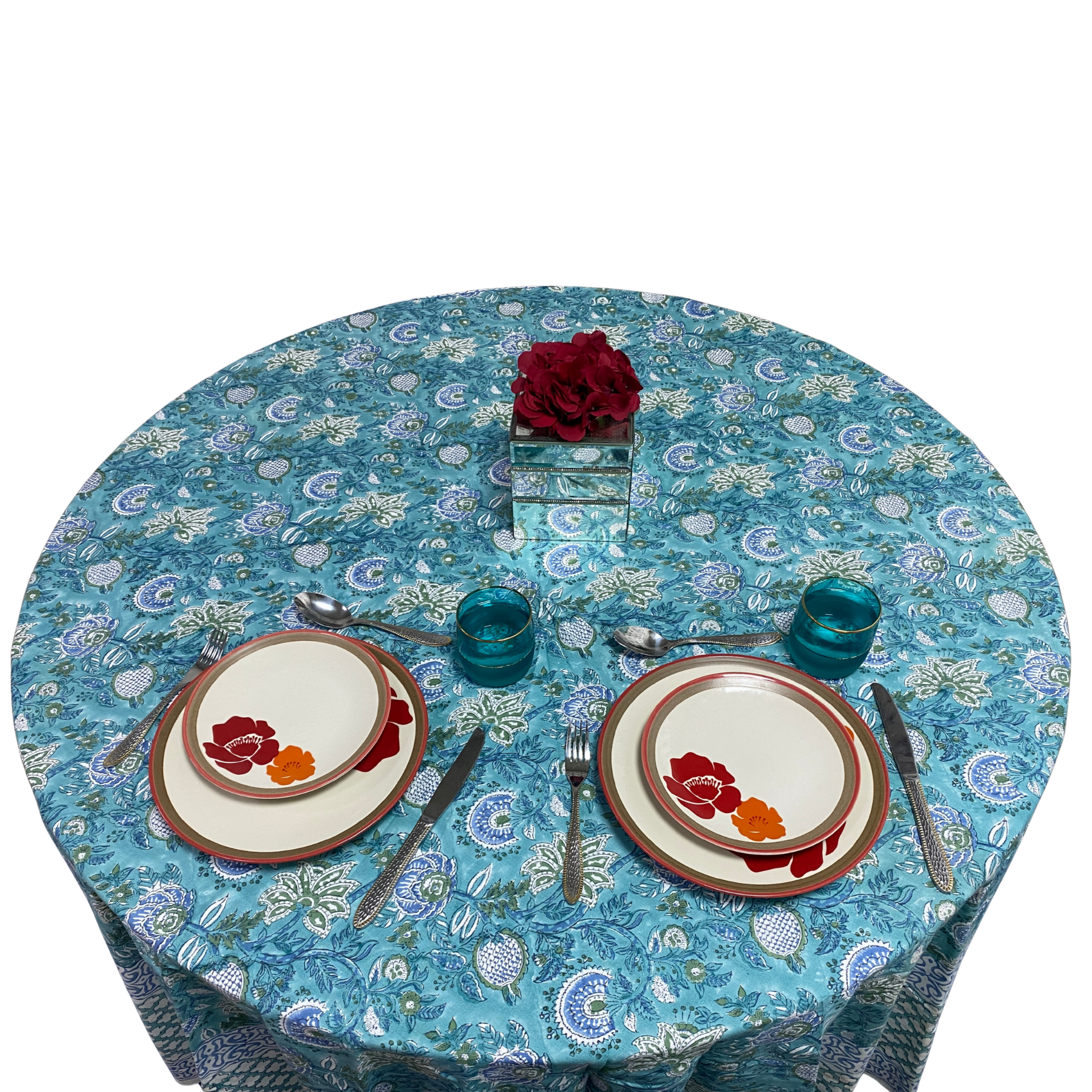 Round table with floral tablecloth, plates, and glasses on a white background
