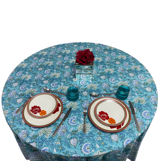 Round table with floral tablecloth, plates, and glasses on a white background