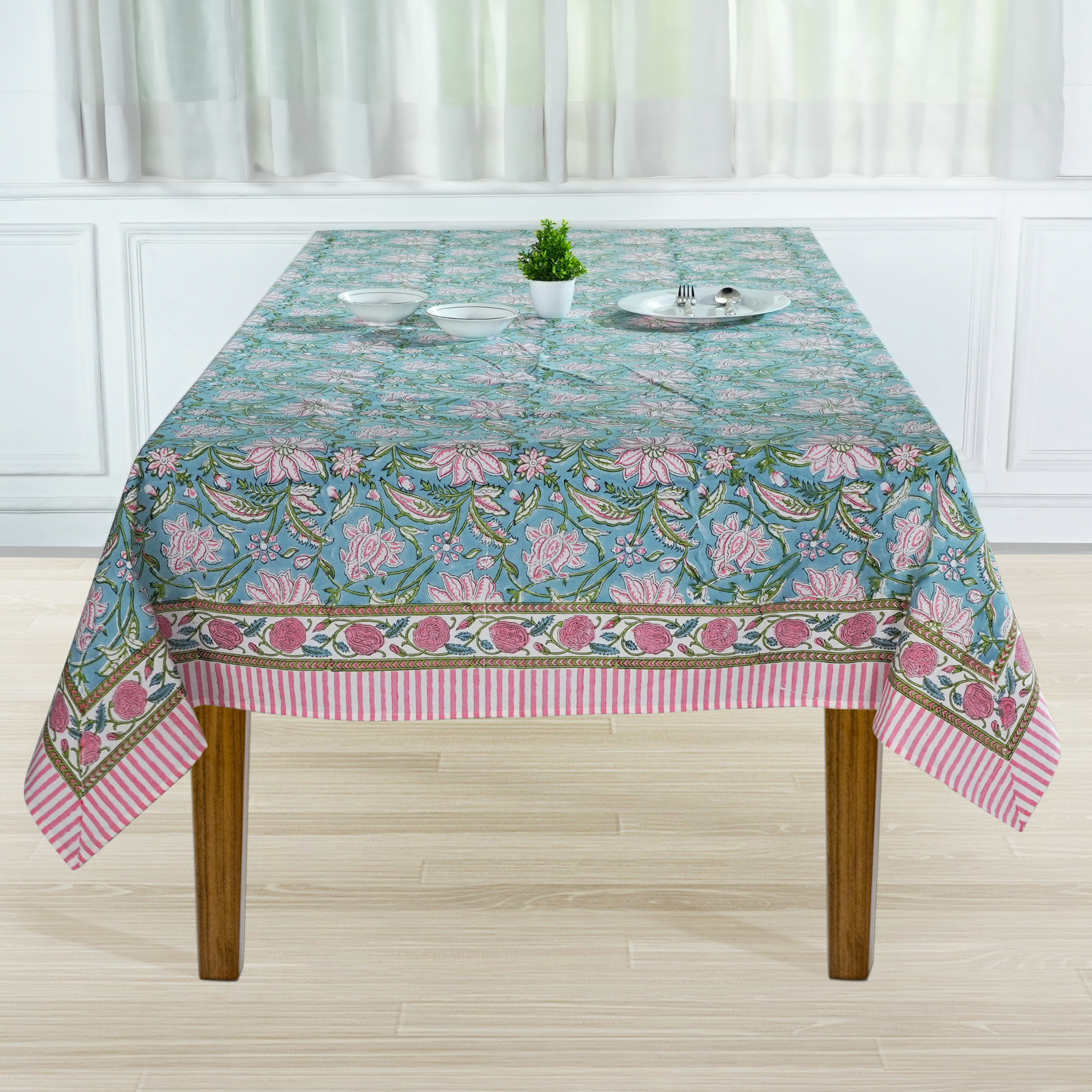 Tablecloth with floral pattern on a wooden table in a room with white curtains.