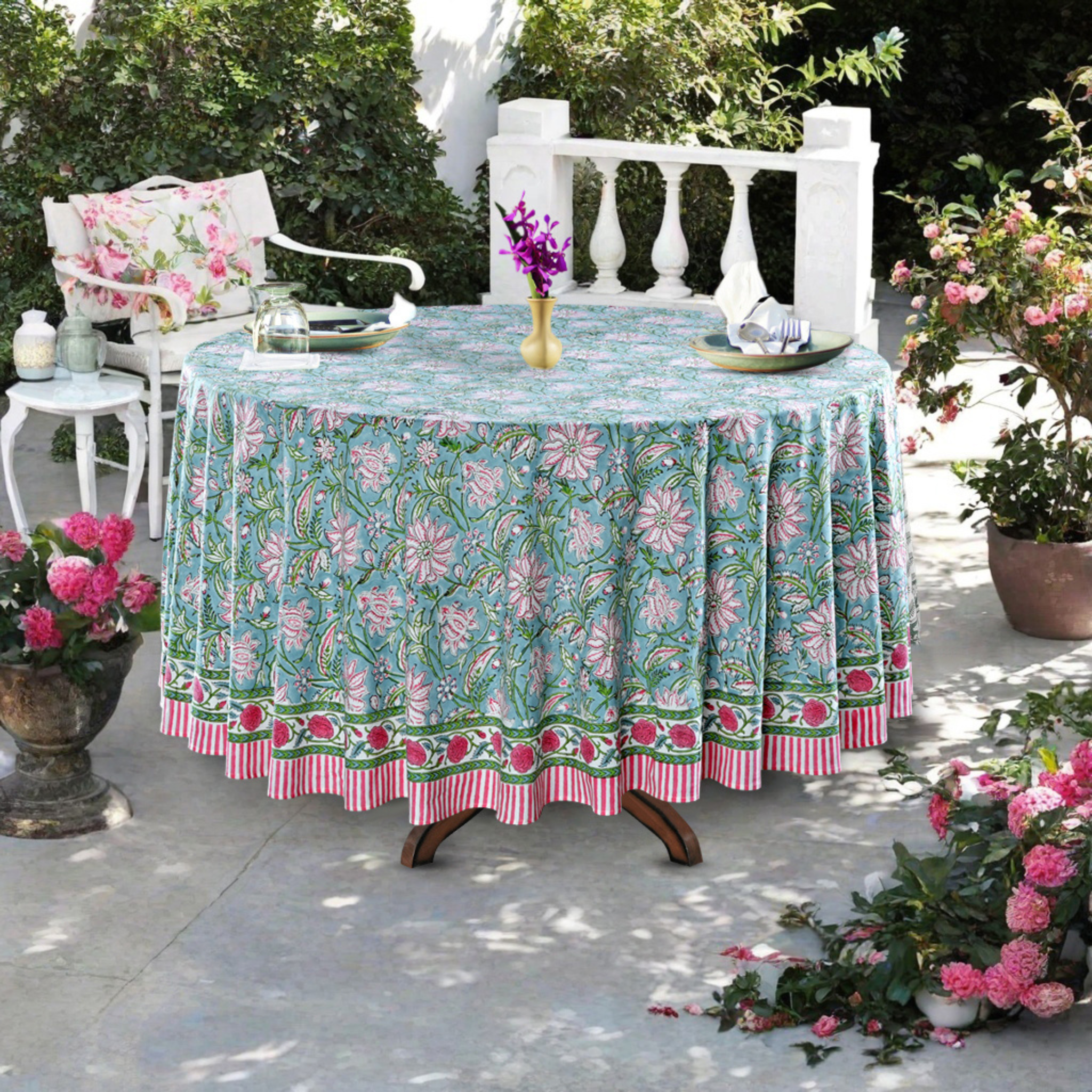 Outdoor table setting with a floral tablecloth, chairs, and decorative elements.