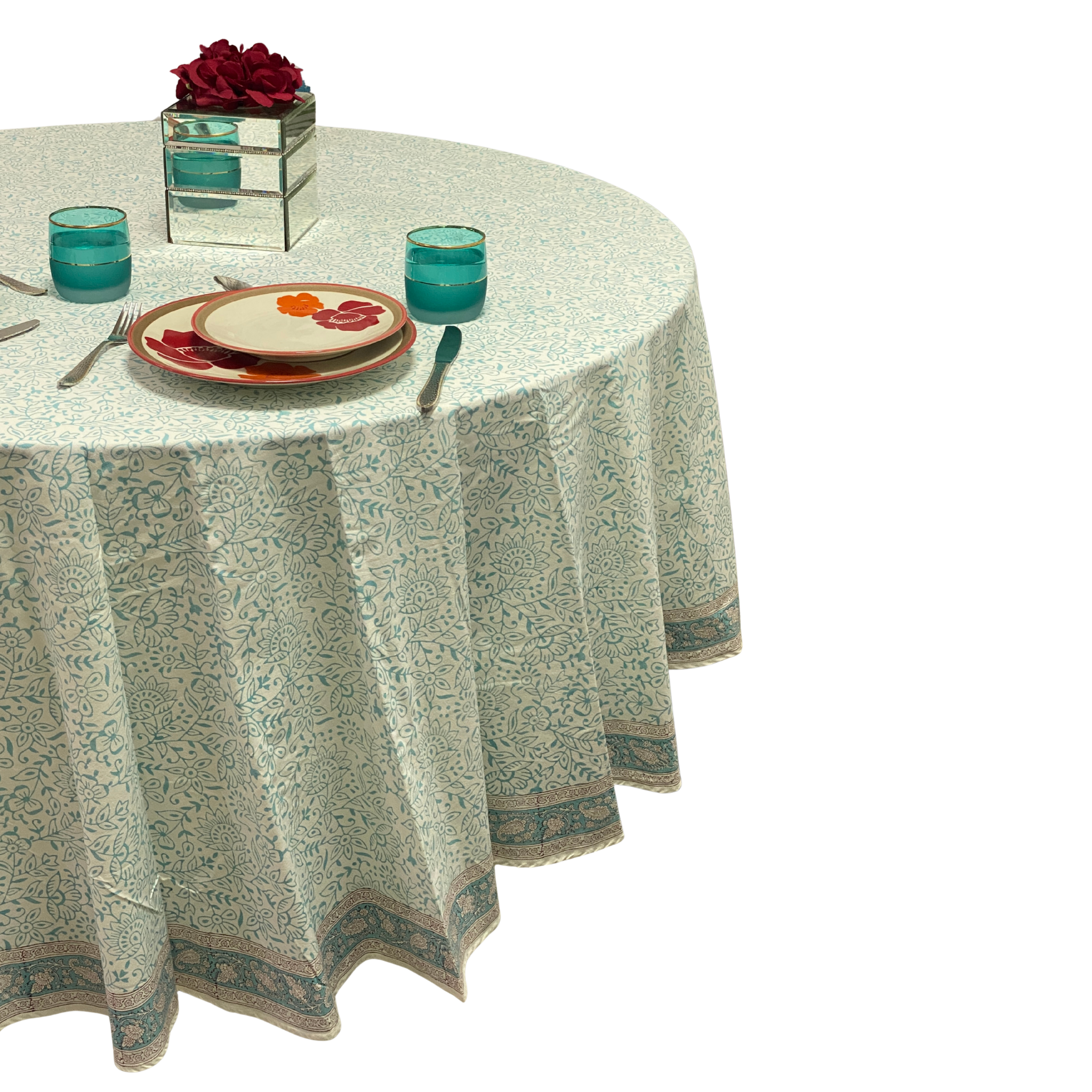 Round table with a patterned tablecloth, plates, glasses, and cutlery on a white background