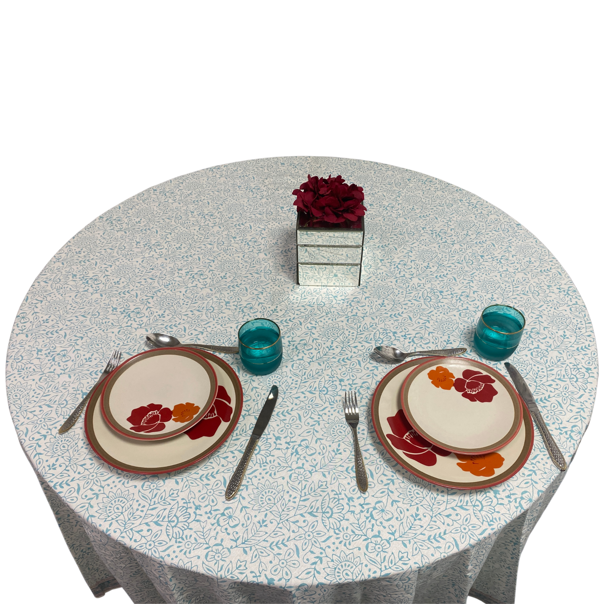 Dining table setting with floral plates, glasses, and cutlery on a patterned tablecloth.
