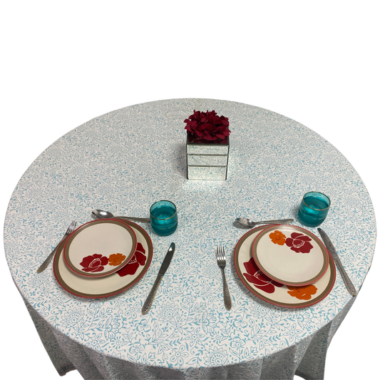 Dining table setting with floral plates, glasses, and cutlery on a patterned tablecloth.