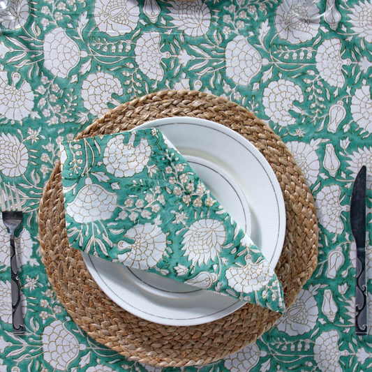 Teal and white floral patterned napkin on a woven placemat over a matching tablecloth.