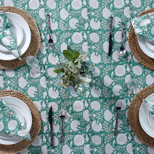 Table setting with floral tablecloth, plates, cutlery, and glasses on a green and white patterned tablecloth.