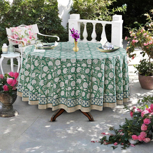 Outdoor setting with a table covered by a green floral-patterned tablecloth, surrounded by potted plants and chairs.