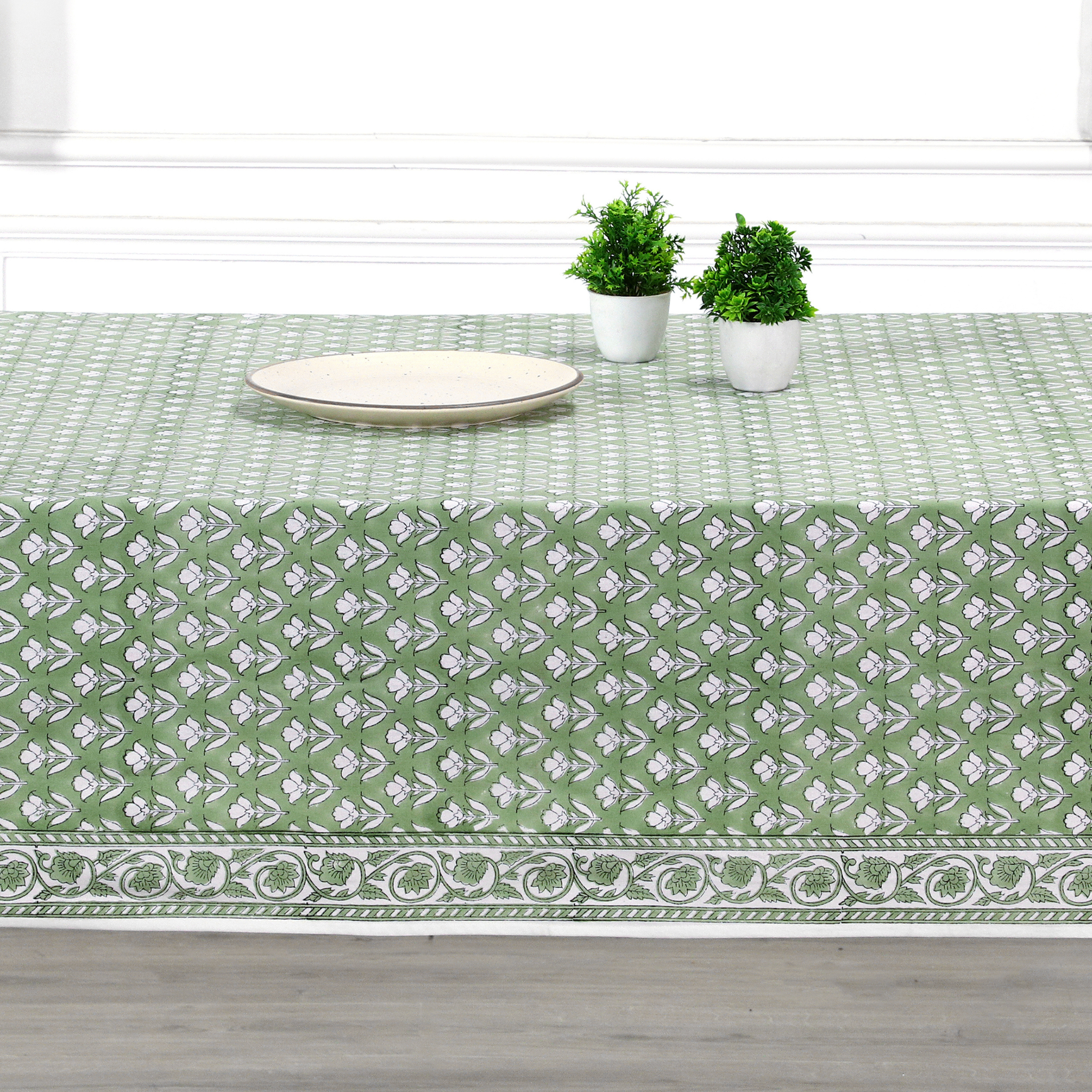 Green and white patterned tablecloth on a wooden table with two potted plants.