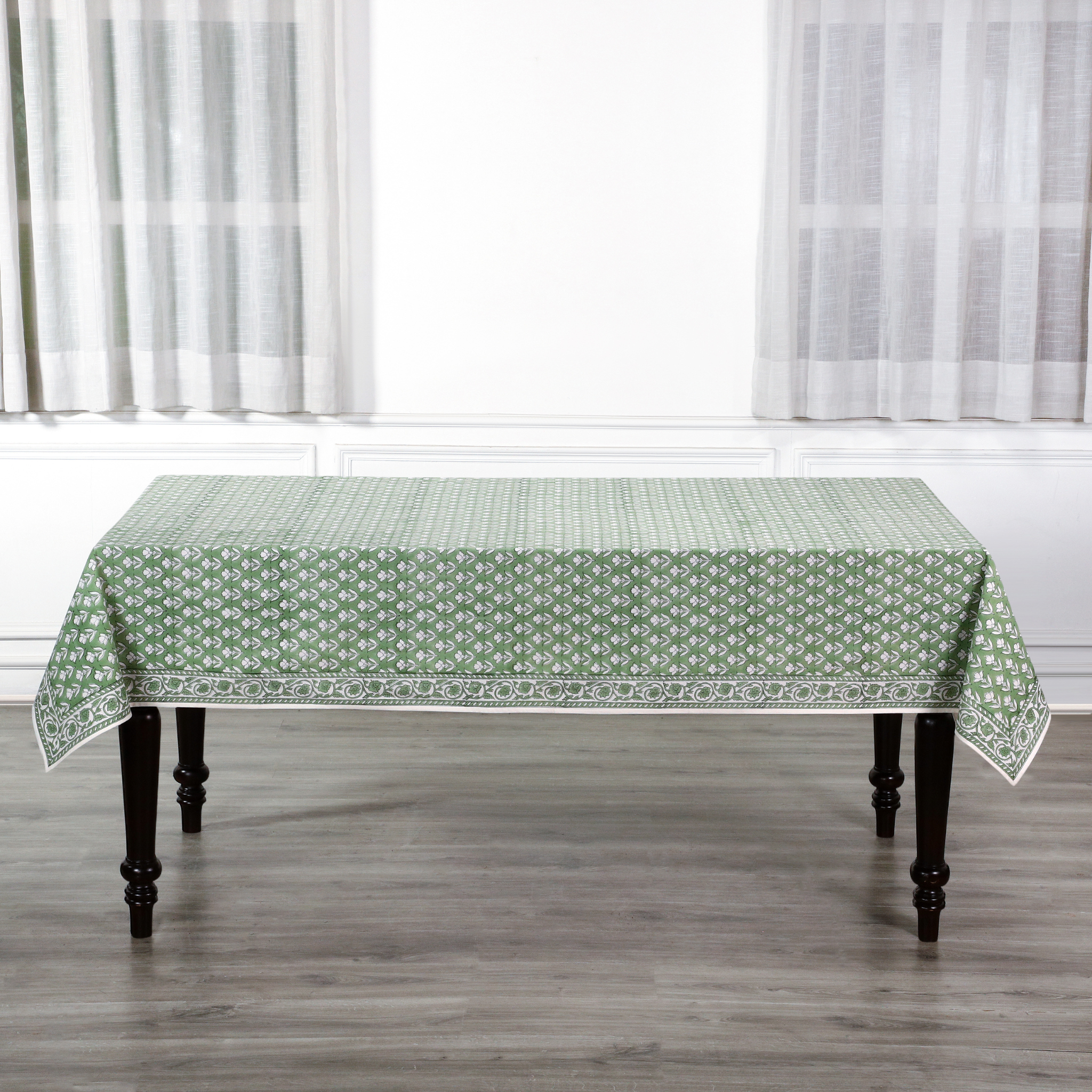 Green patterned tablecloth on a wooden table with white curtains in the background