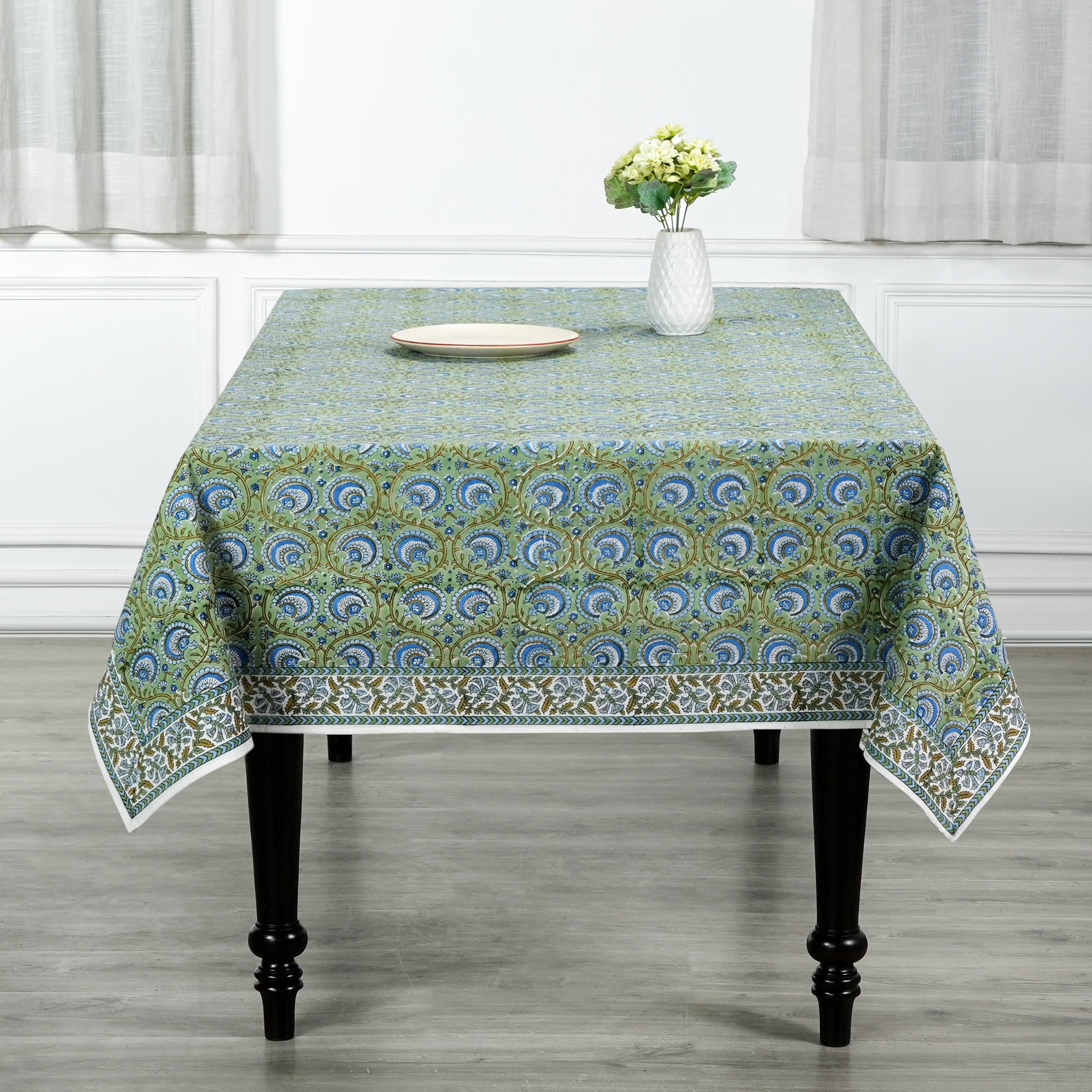 Tablecloth with a green and blue pattern on a table in a room with white curtains.