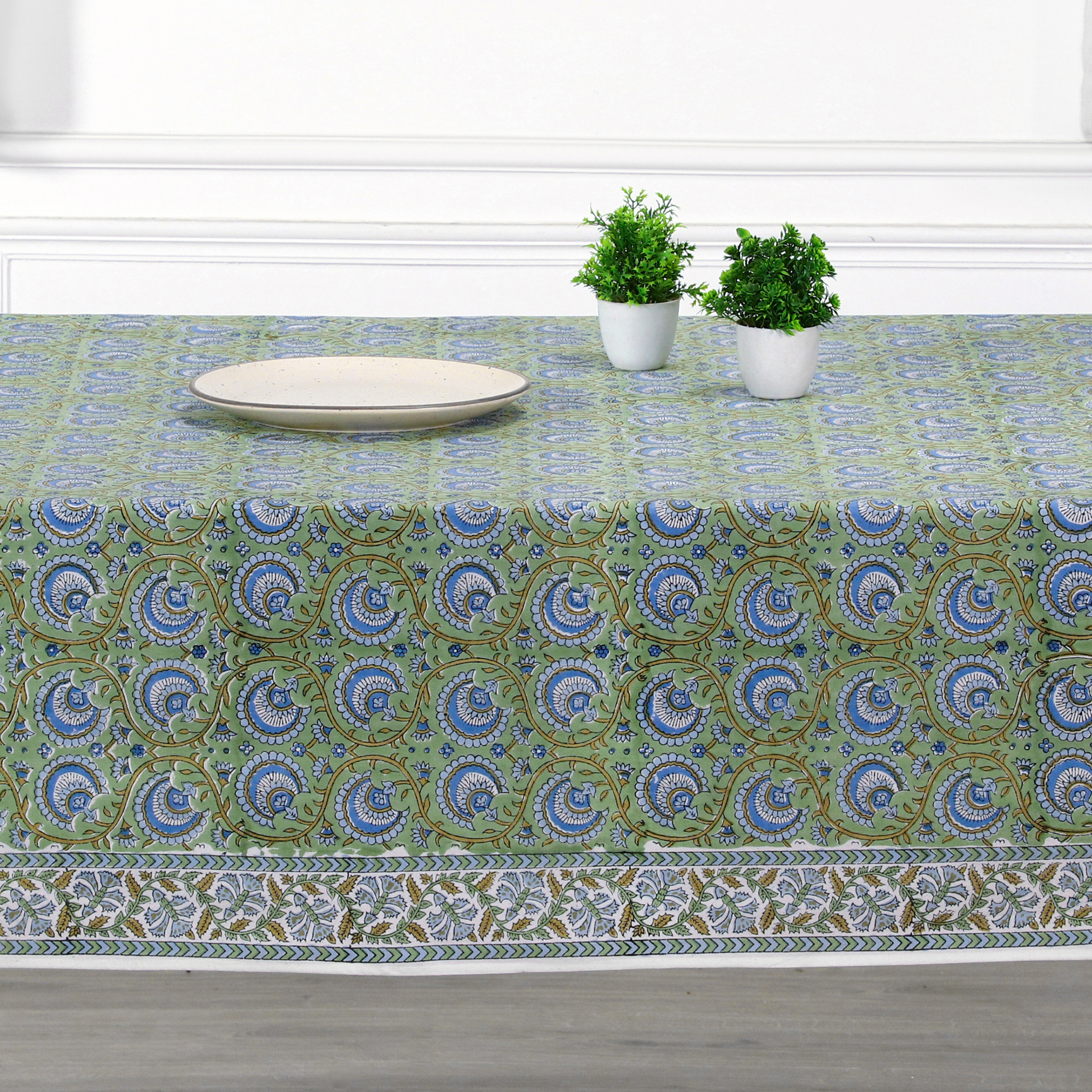 Tablecloth with a green and blue pattern on a table with plates and plants.
