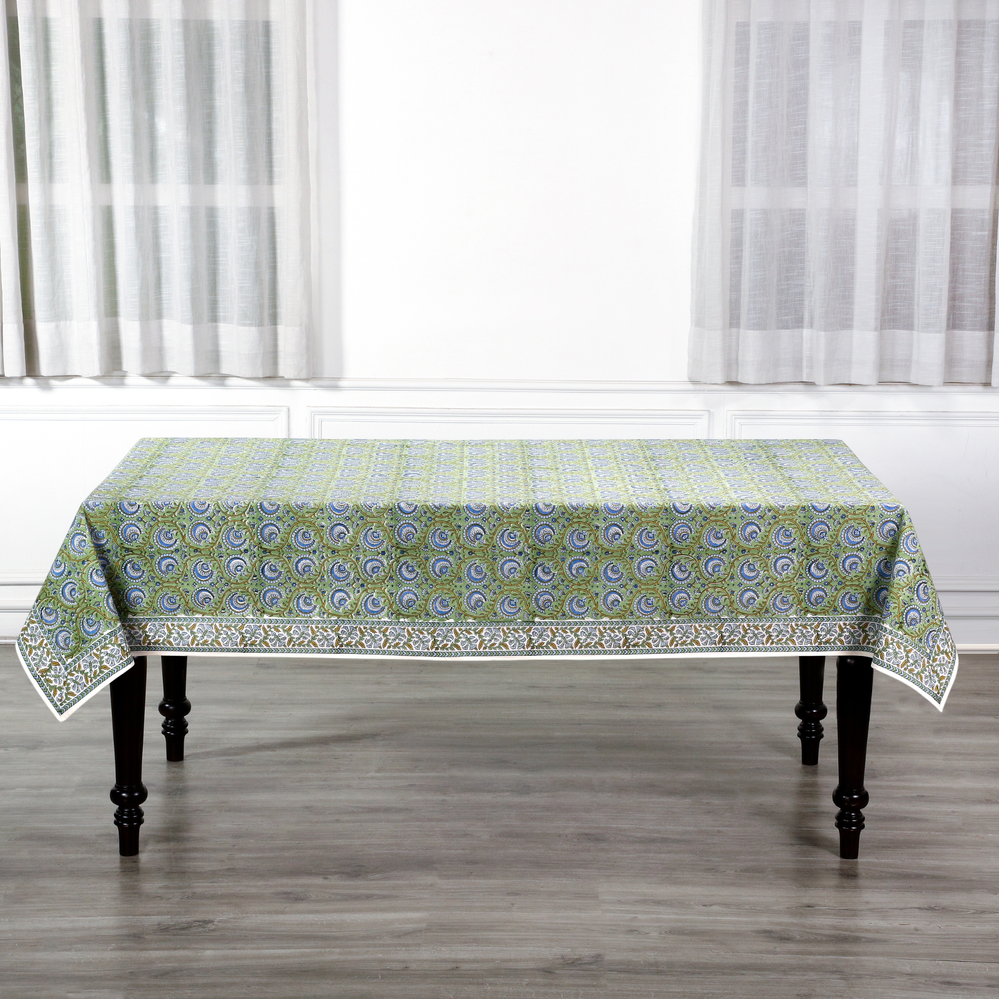 Tablecloth with green and white pattern on a wooden table in a room with white curtains.