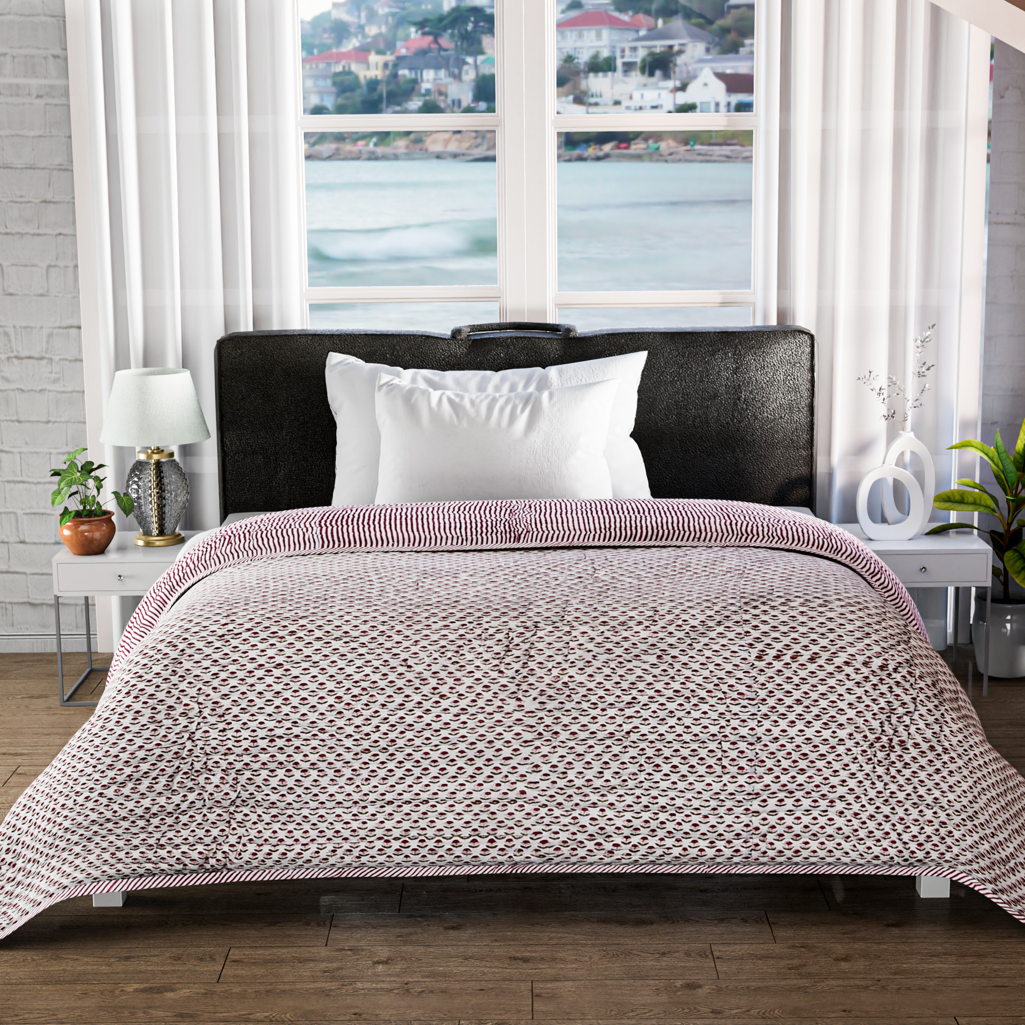 Bed with pink and white patterned comforter in a room with large windows showing a waterfront view.