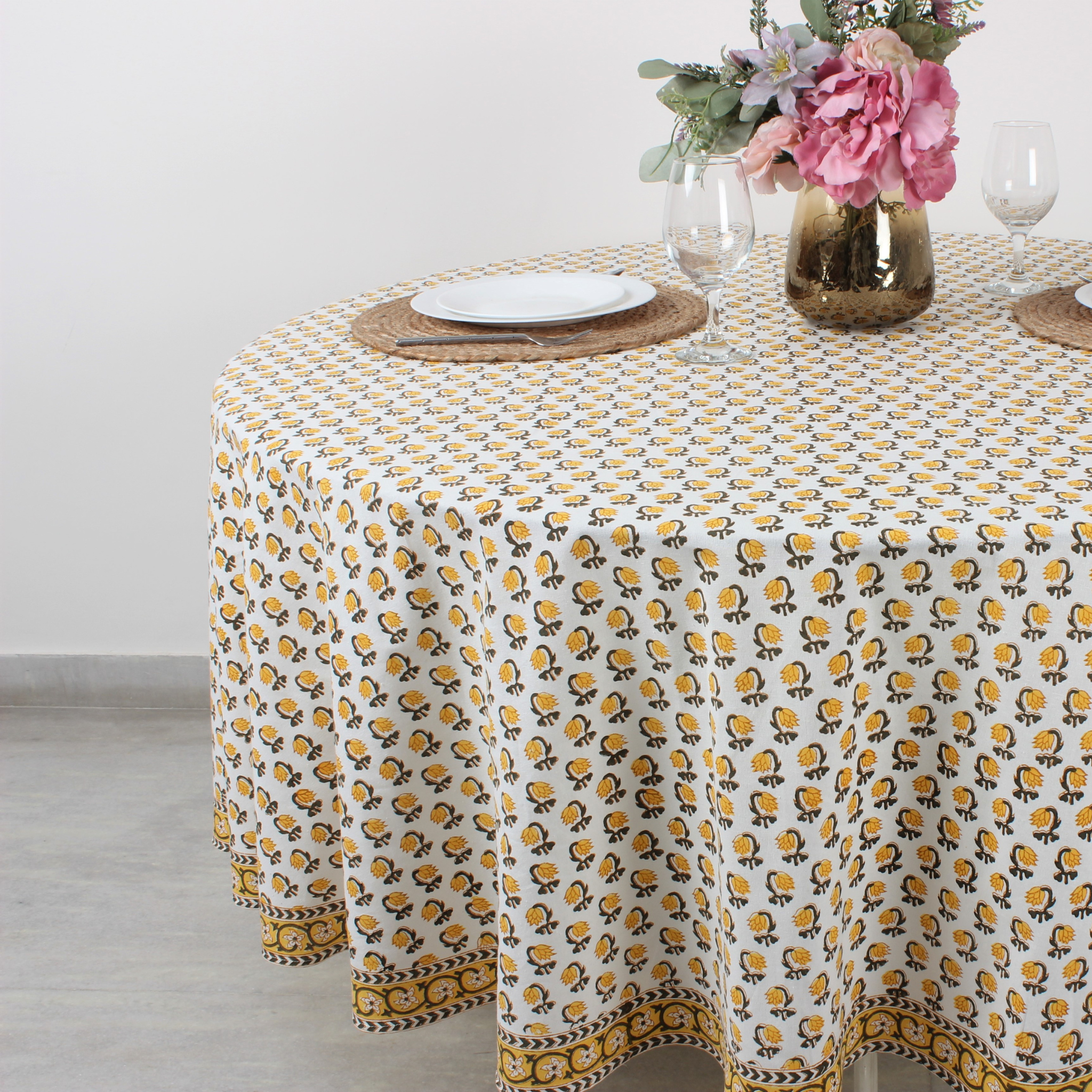 Round table with a patterned tablecloth, plates, and flowers on a light background