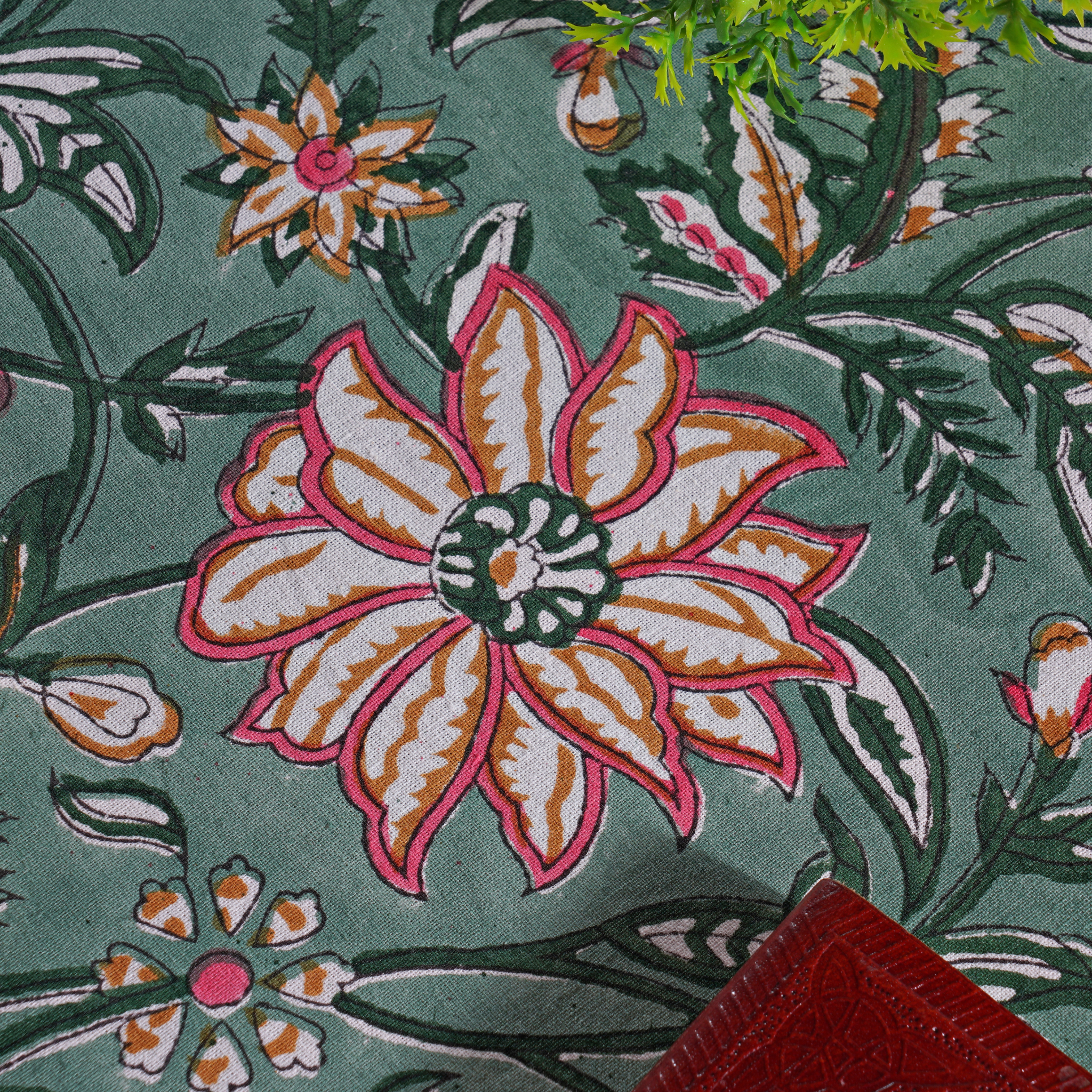Close-up of a floral patterned fabric with pink and orange flowers on a green background.